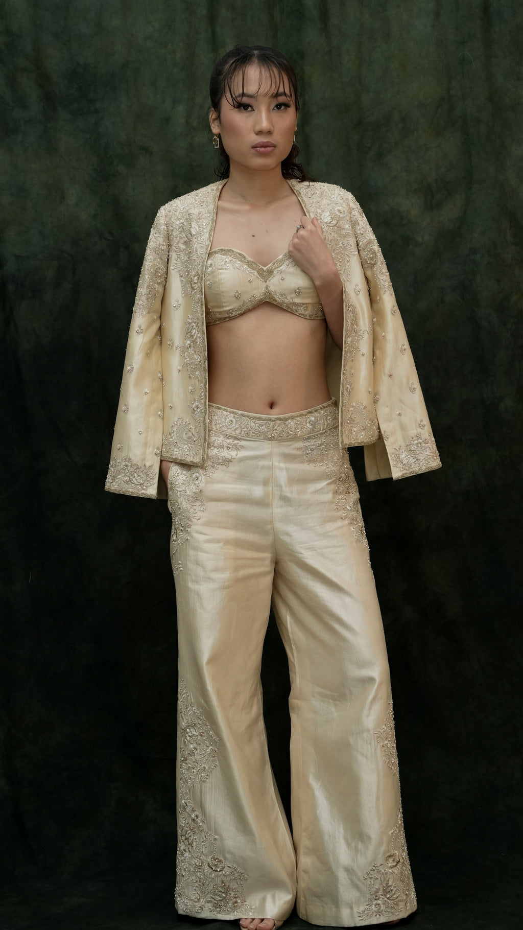 Woman wearing a beige embroidered outfit against a dark background