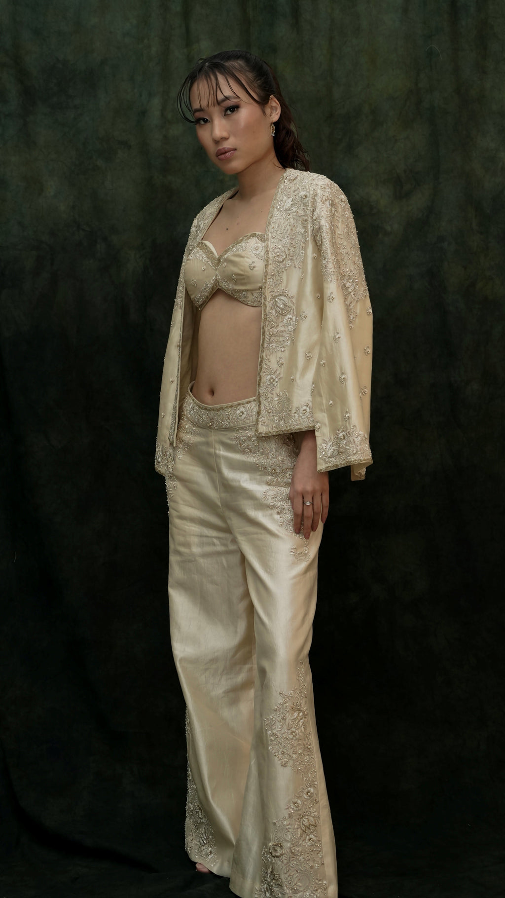 Woman wearing a beige embroidered outfit against a dark background