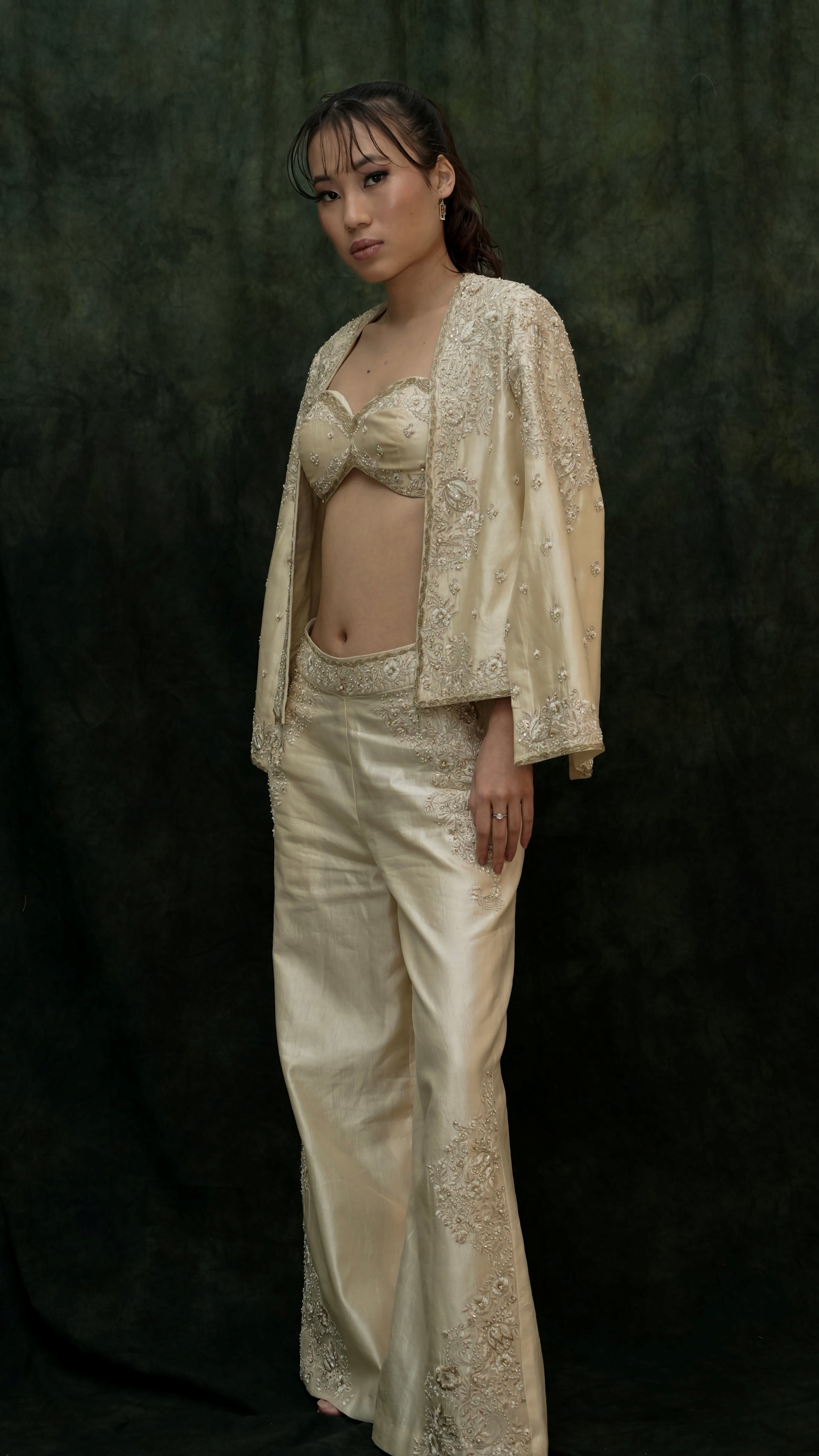 Woman wearing a beige embroidered outfit against a dark background