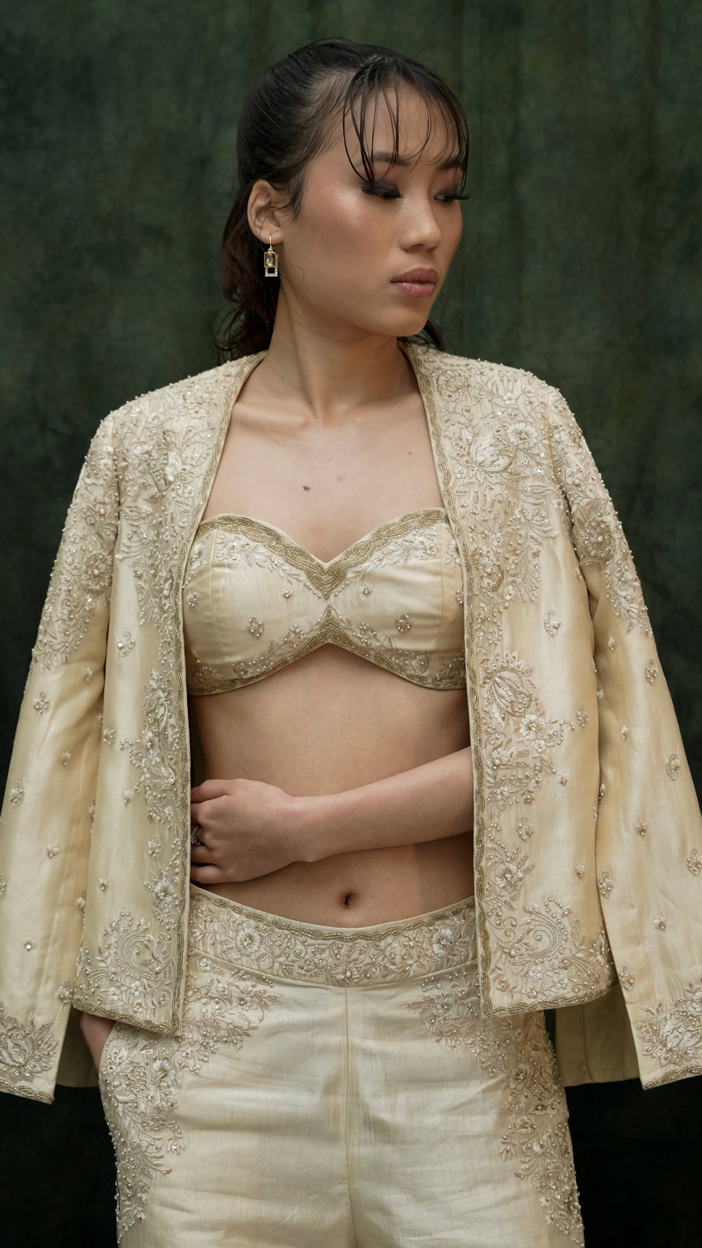 Woman wearing a beige embroidered outfit against a dark background