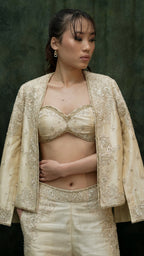 Woman wearing a beige embroidered outfit against a dark background