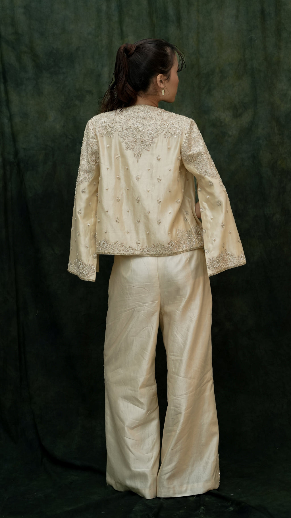 Person wearing a beige embroidered jacket and pants against a dark green background