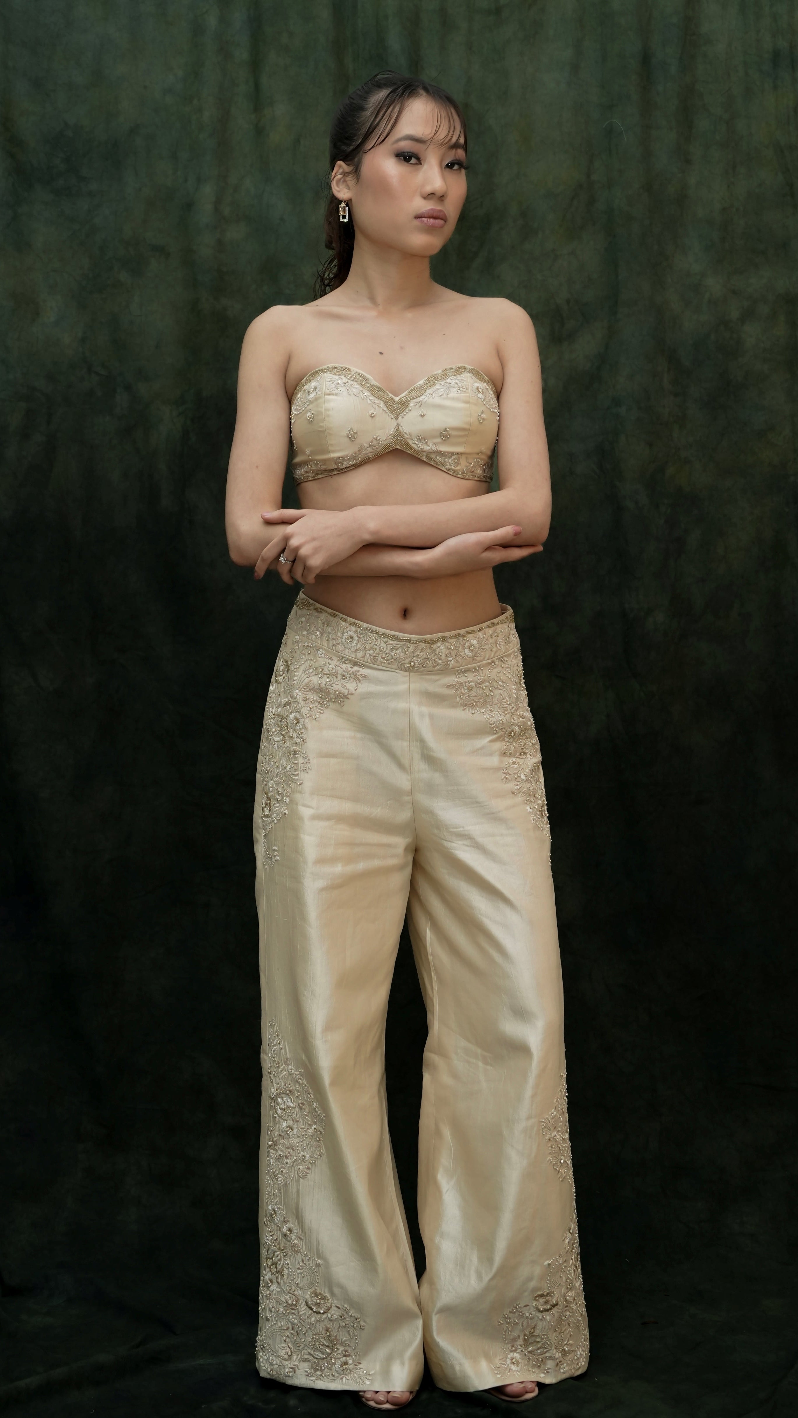 Woman wearing a beige embroidered outfit against a dark background