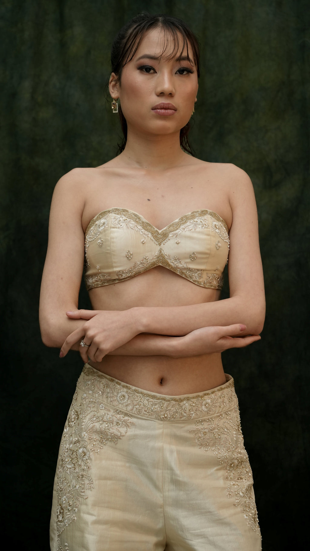 Woman wearing a gold embroidered top and pants against a dark background