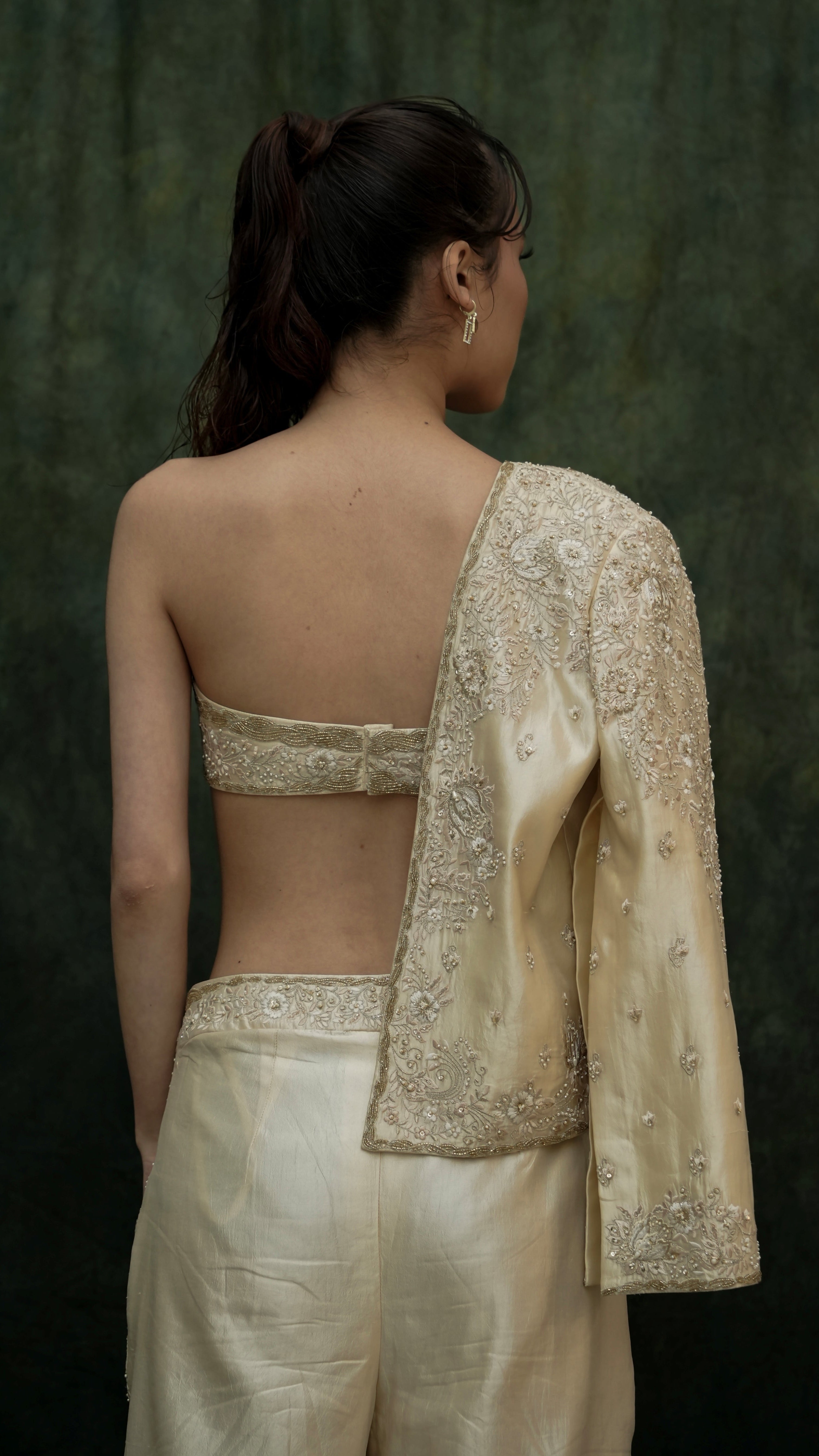 Woman wearing a traditional outfit with a backless top and embroidered jacket against a dark background
