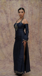 Woman in a dark blue evening gown with gold detailing against a textured wall.