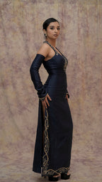 Woman wearing a black evening gown with gold embroidery against a textured beige background