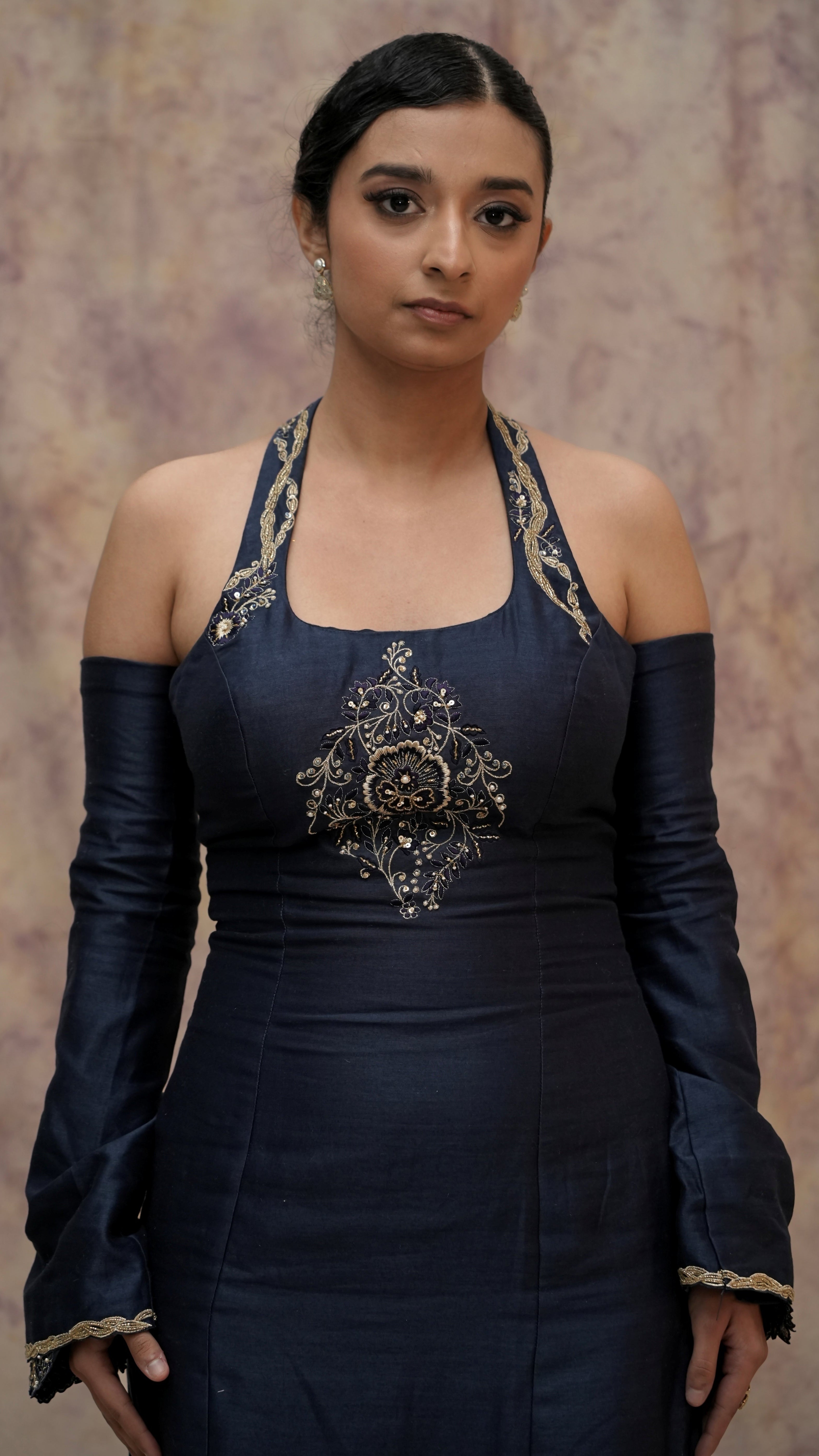 Woman wearing a dark blue traditional outfit with intricate designs against a neutral background