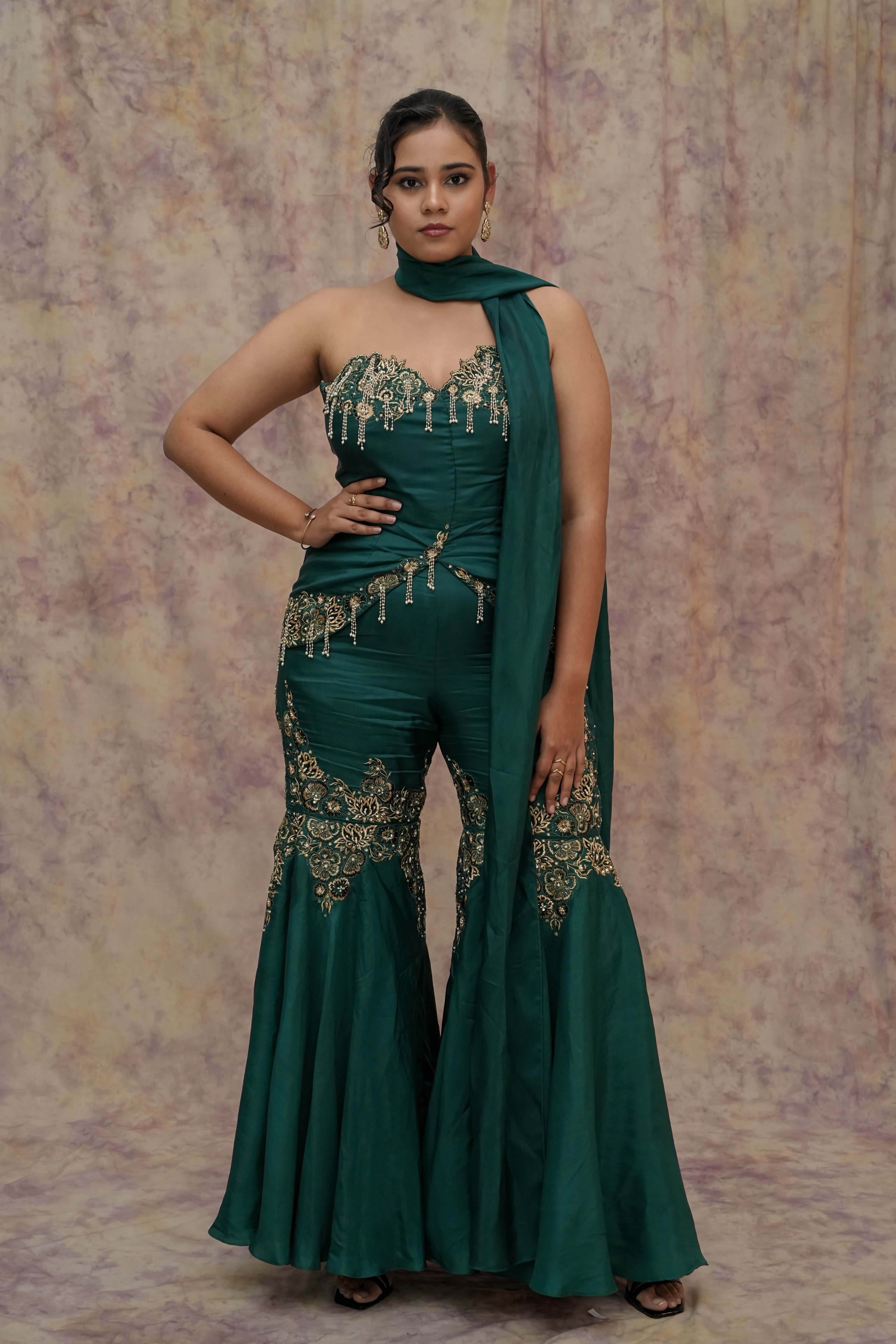 Woman in a green traditional outfit with intricate designs against a textured background