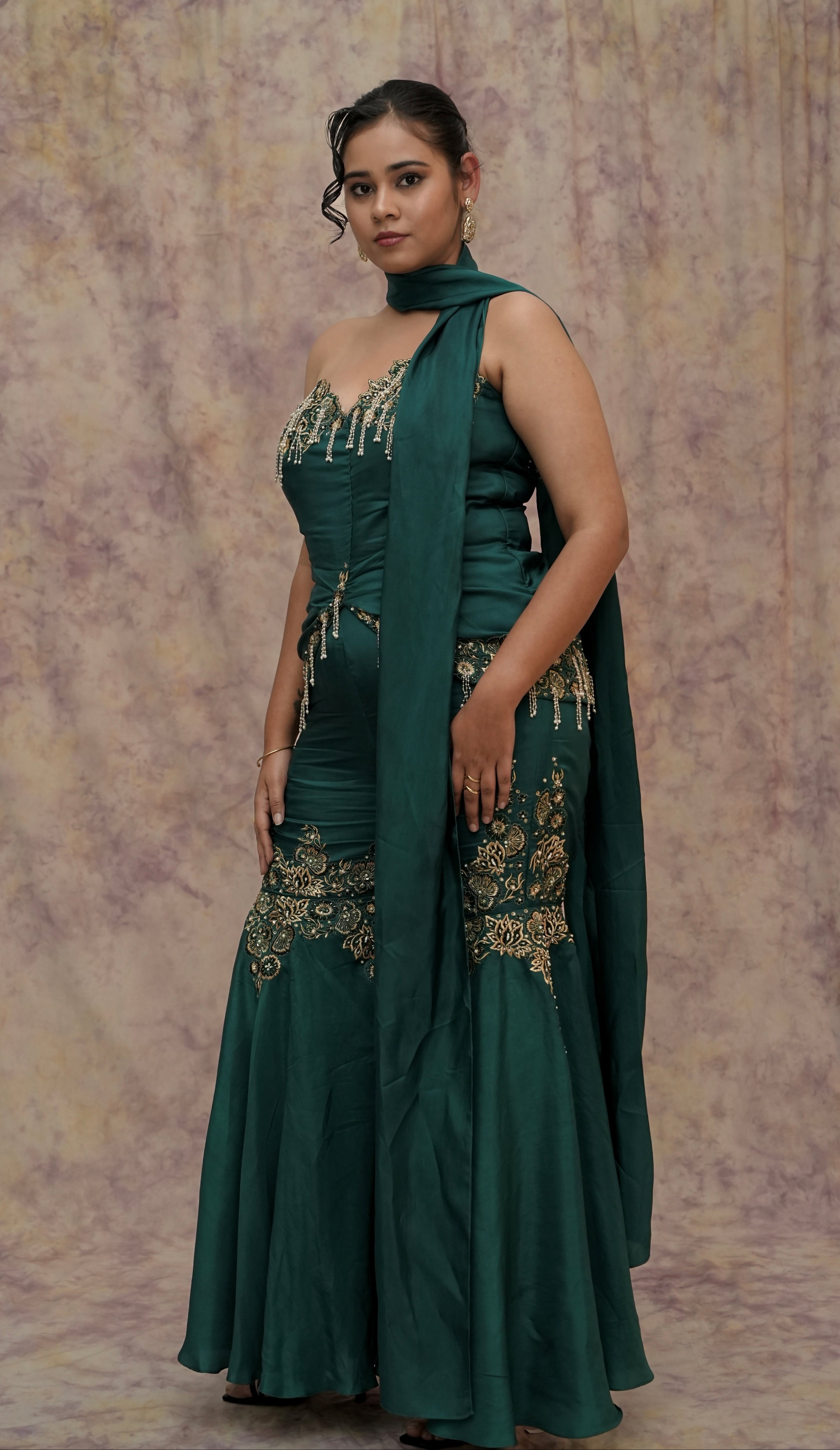 Woman wearing a green traditional outfit with gold embroidery against a textured beige background