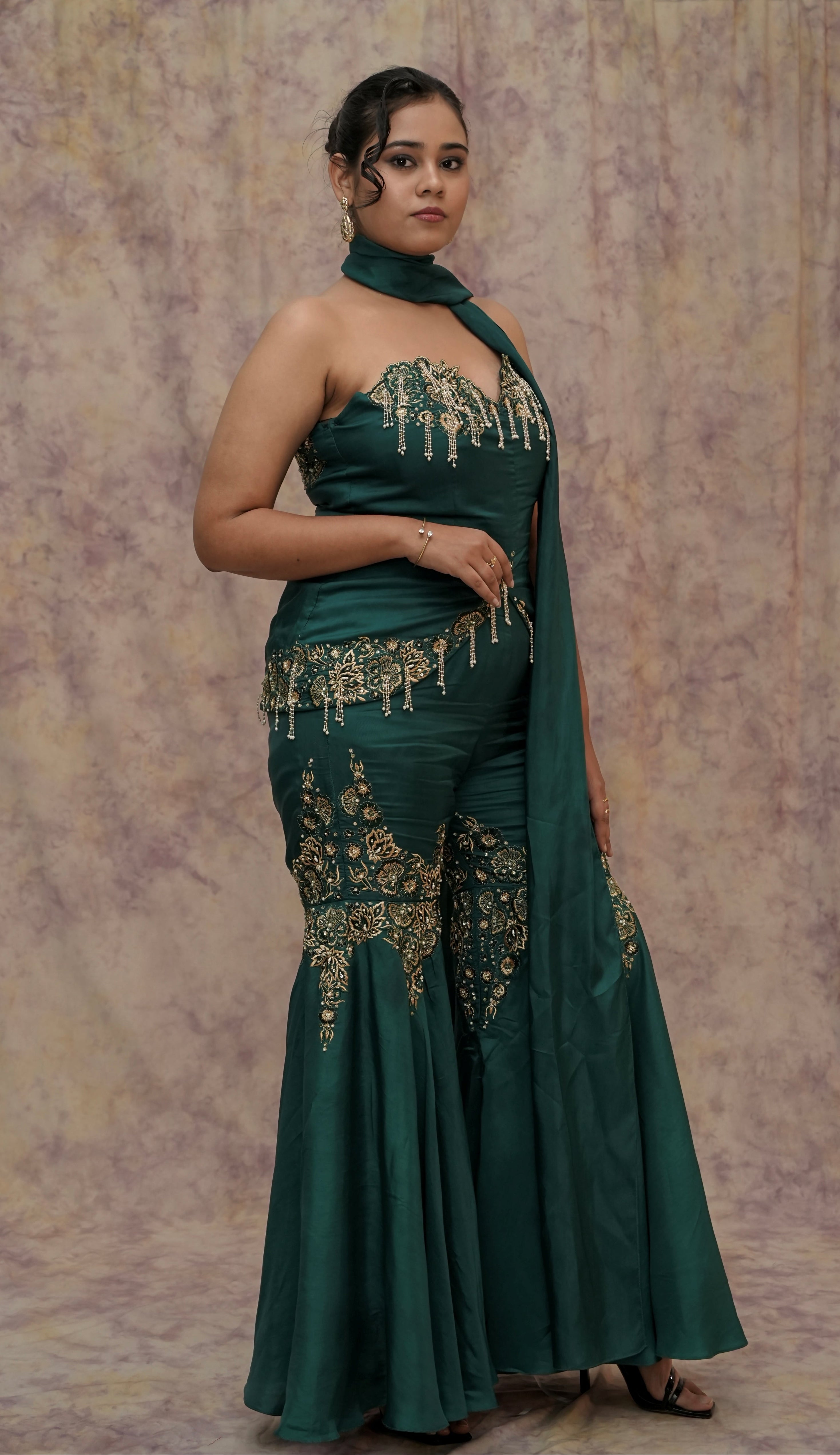 Woman wearing a green embroidered saree with a matching blouse against a textured beige background