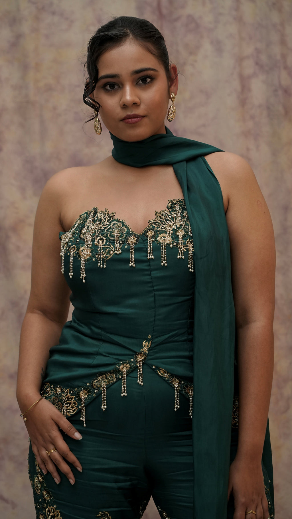Woman wearing a green outfit with gold embellishments against a plain background