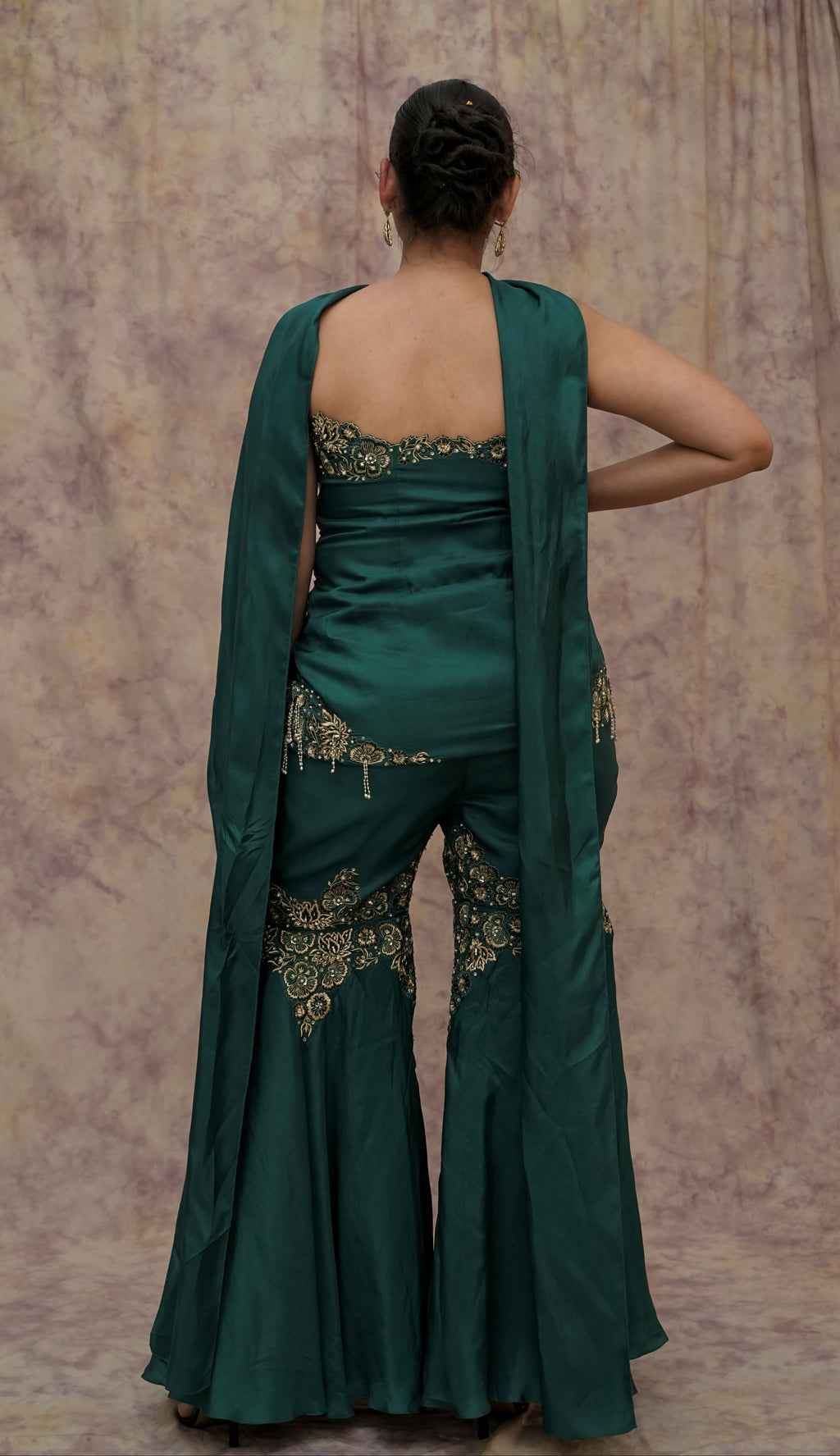 Woman wearing a green saree with gold embroidery against a textured wall.