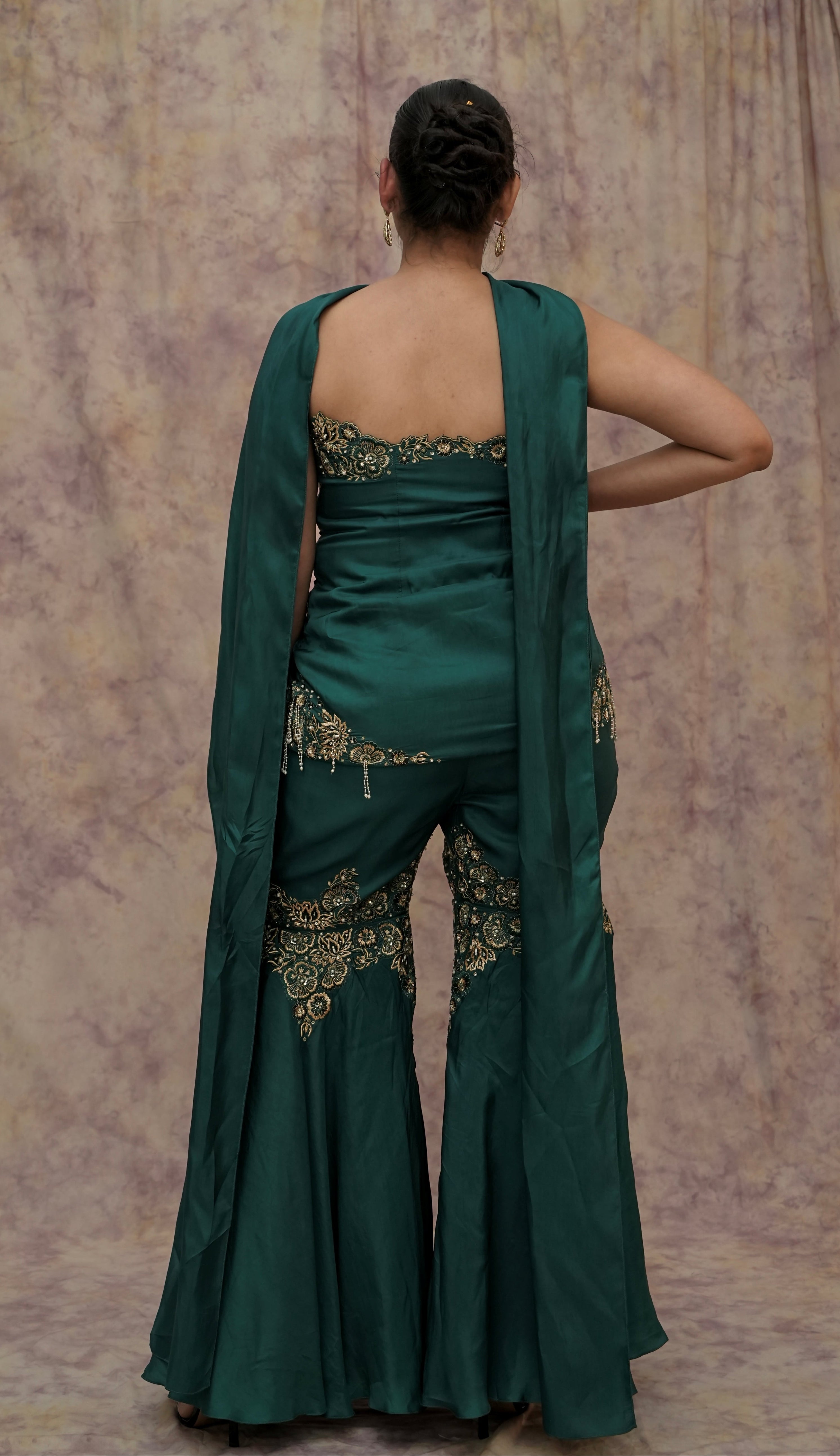 Woman wearing a green saree with gold embroidery against a textured wall.