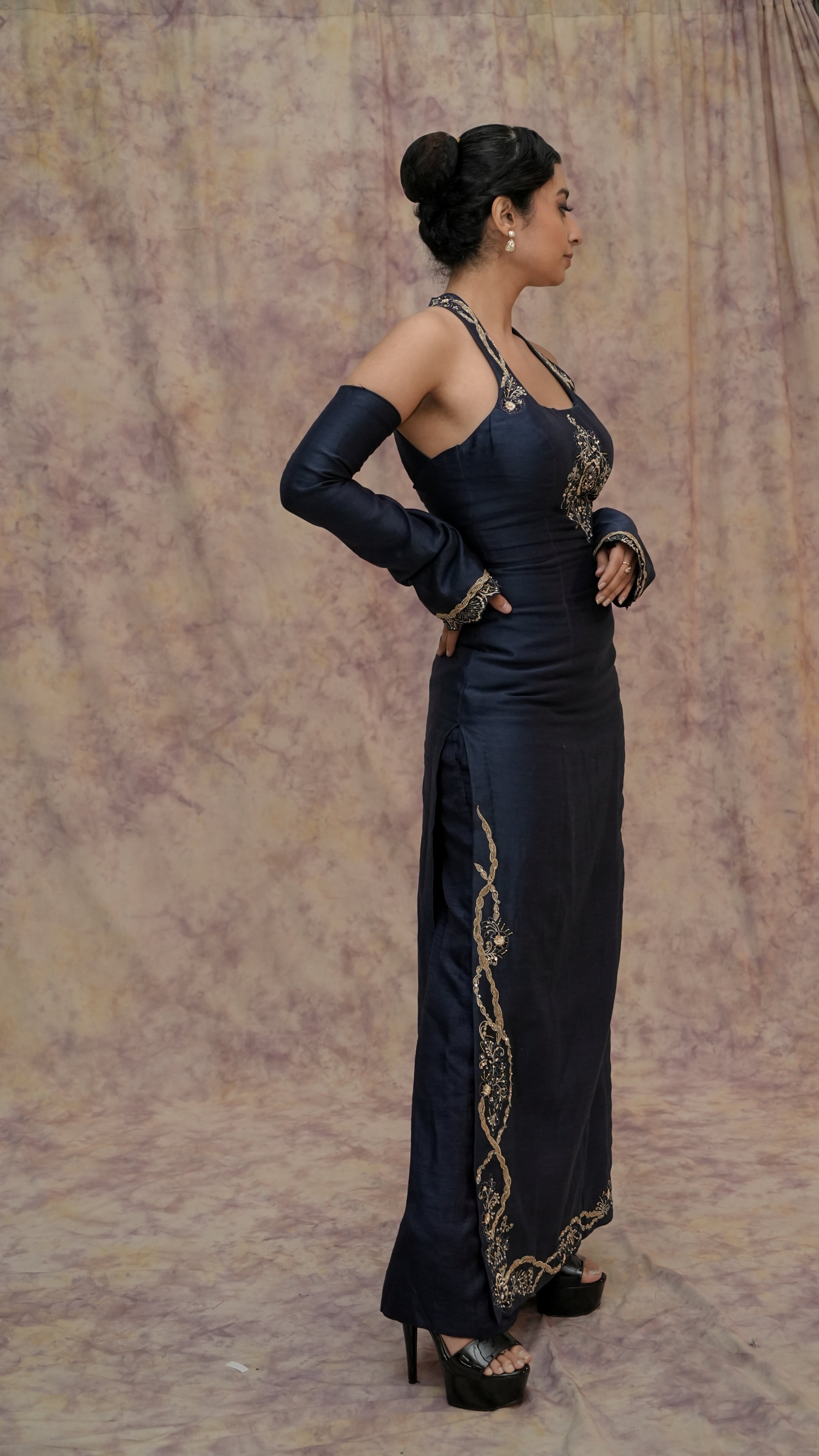 Woman in a black evening gown with gold detailing against a textured beige background