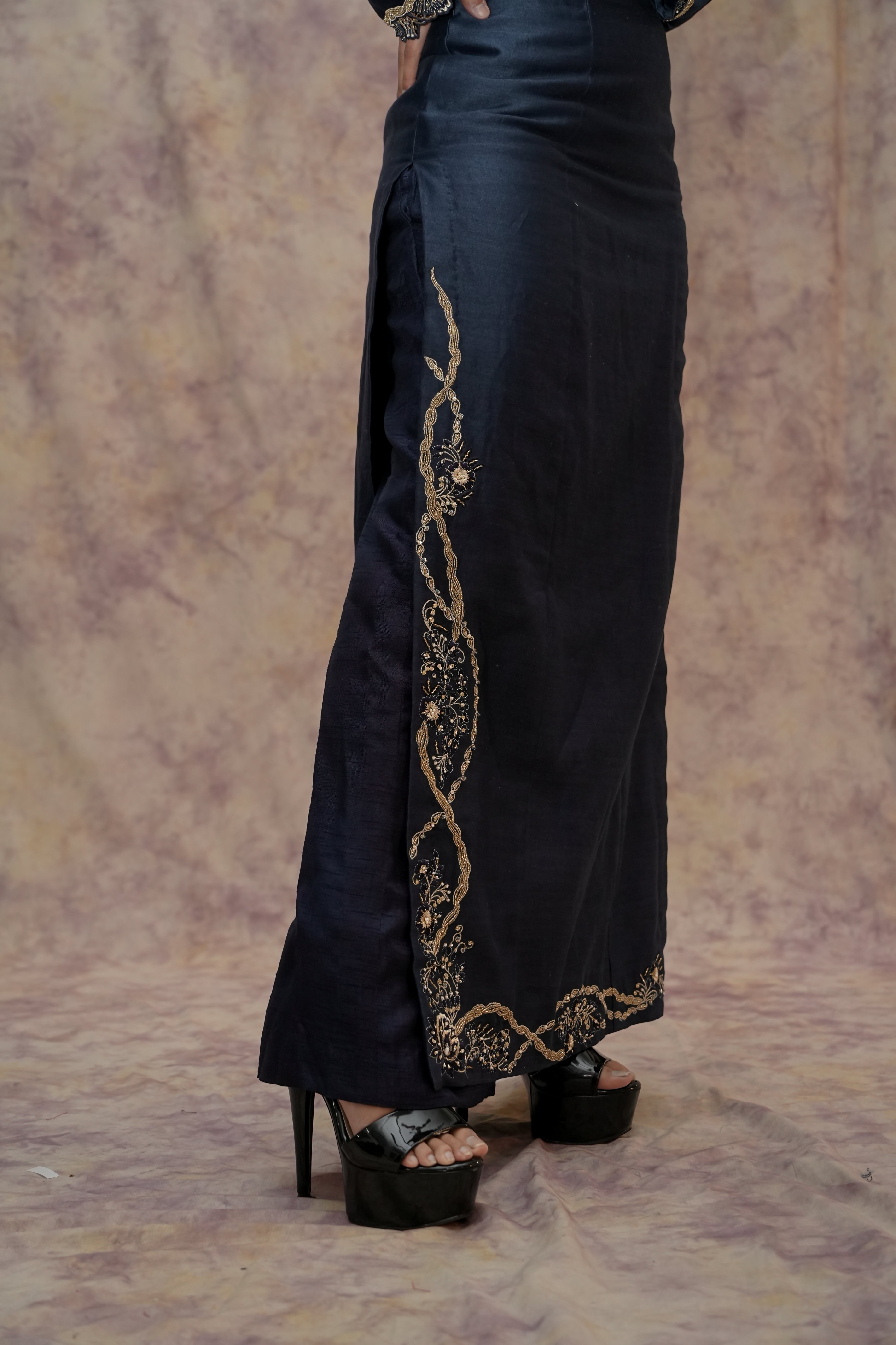 Black pants with gold embroidery worn by a person on a patterned background