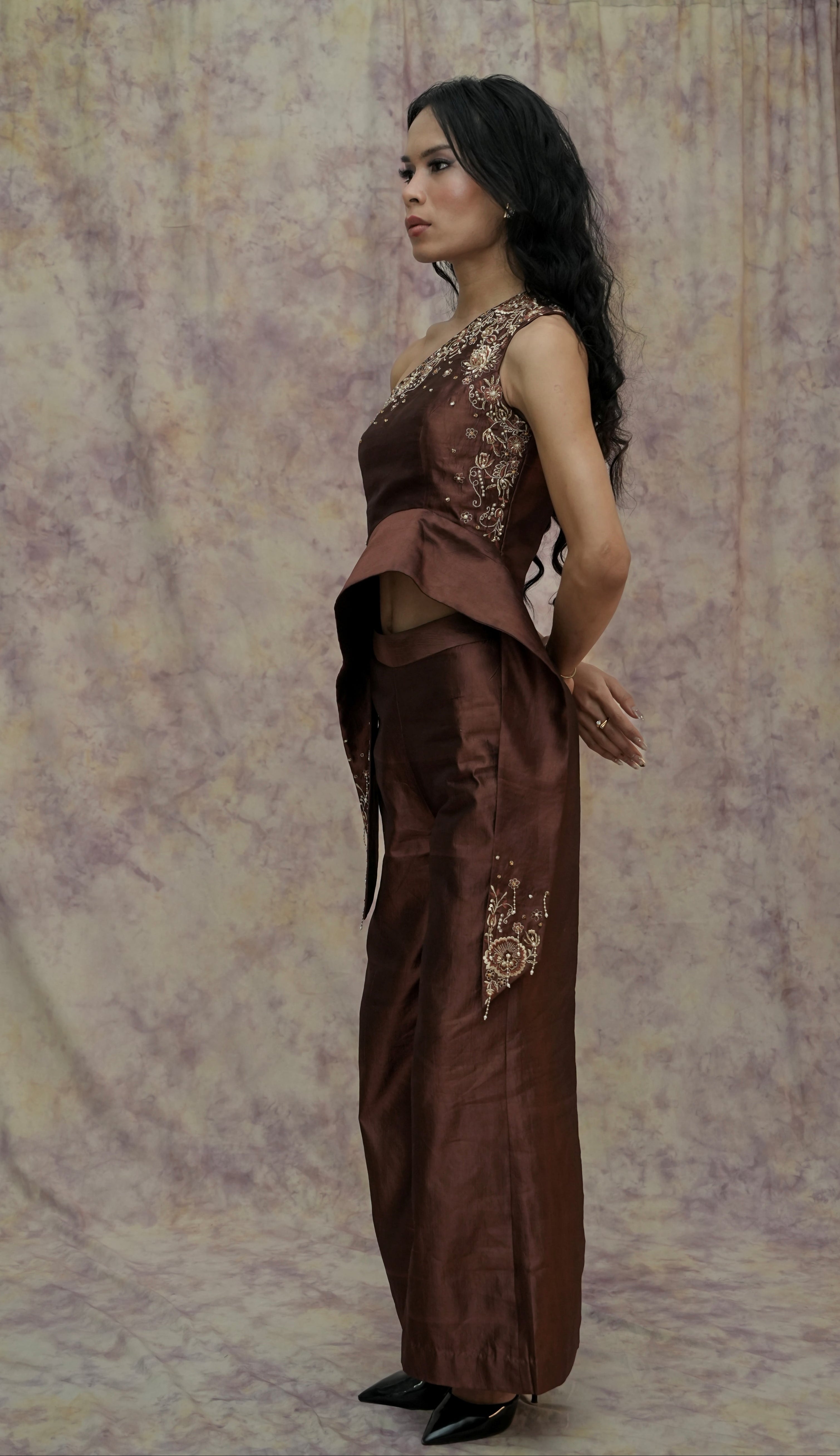 Woman wearing a brown dress with floral patterns against a patterned curtain background