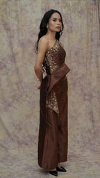 Woman wearing a brown dress with floral patterns against a patterned backdrop
