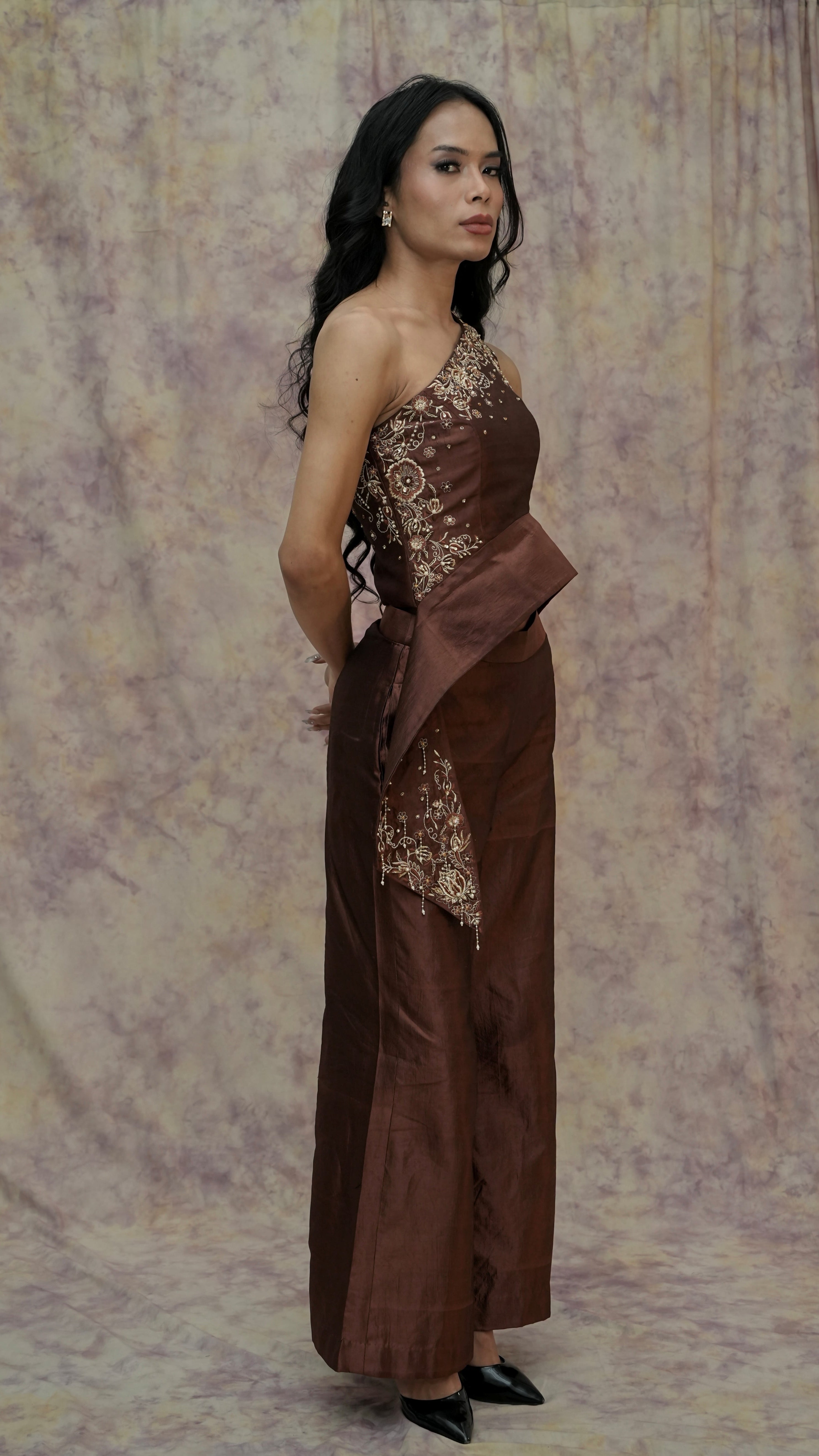 Woman wearing a brown dress with floral patterns against a patterned backdrop