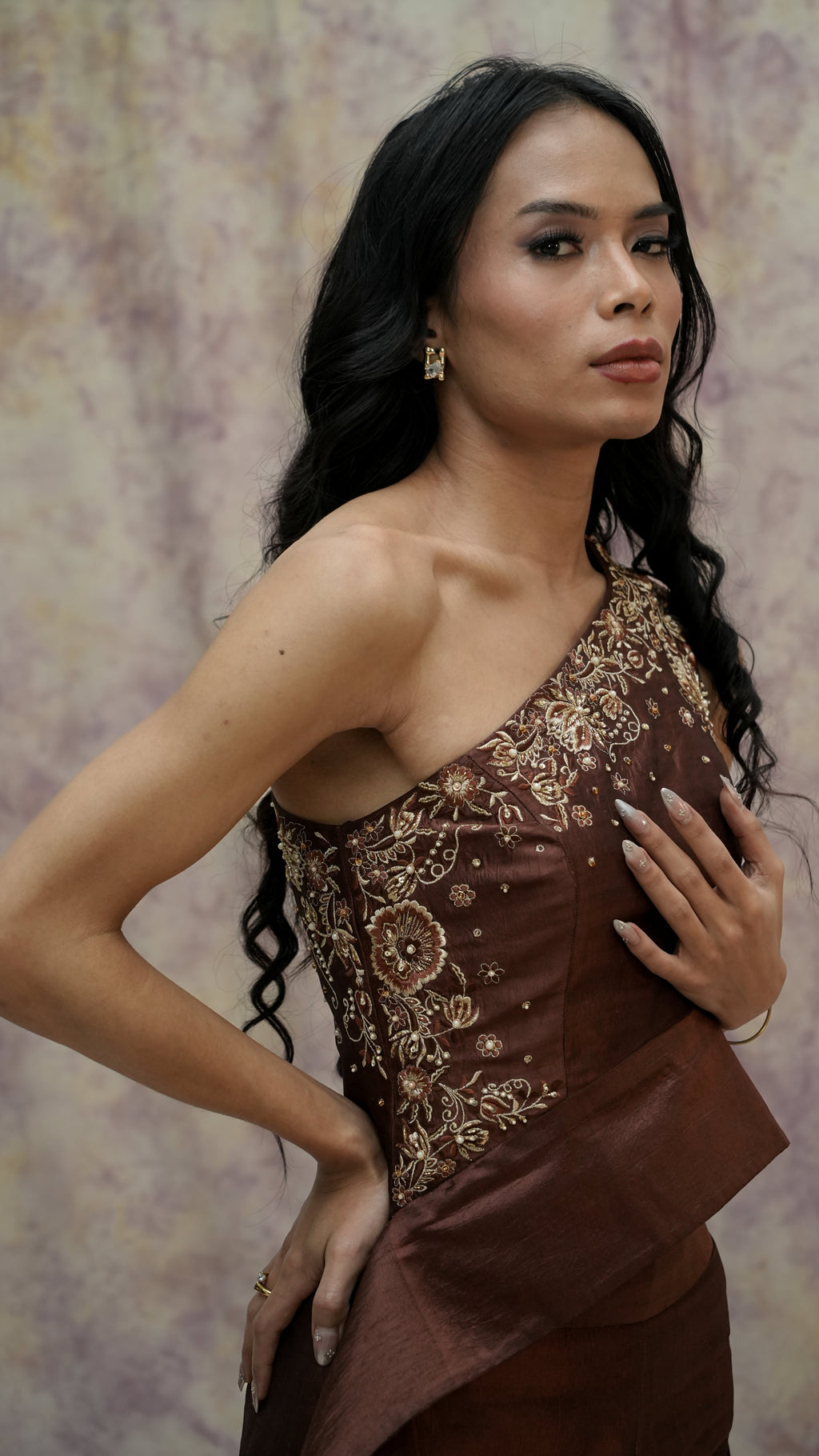 Woman wearing a brown dress with gold embroidery against a patterned background