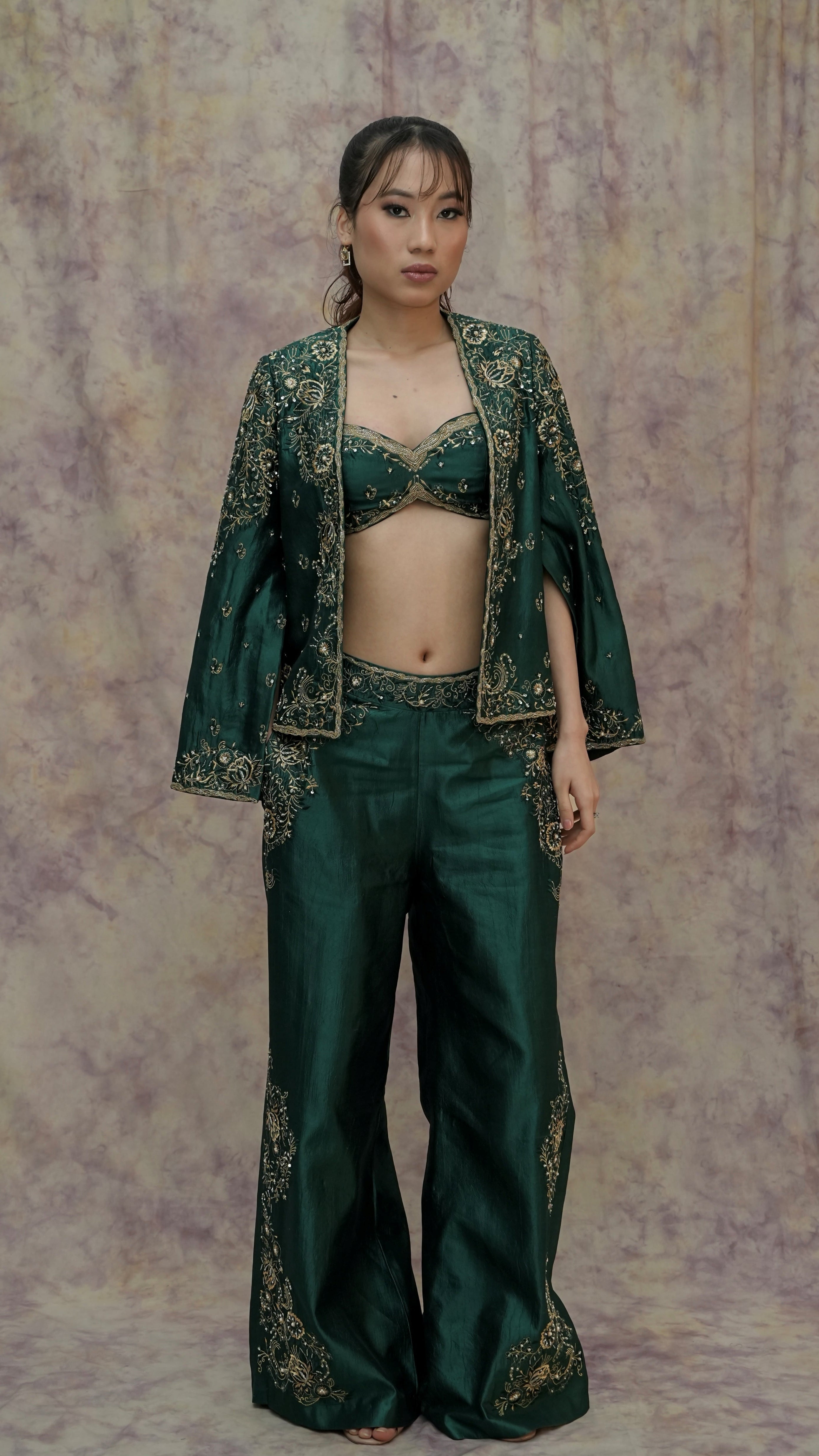 Woman wearing a green embroidered outfit against a patterned background