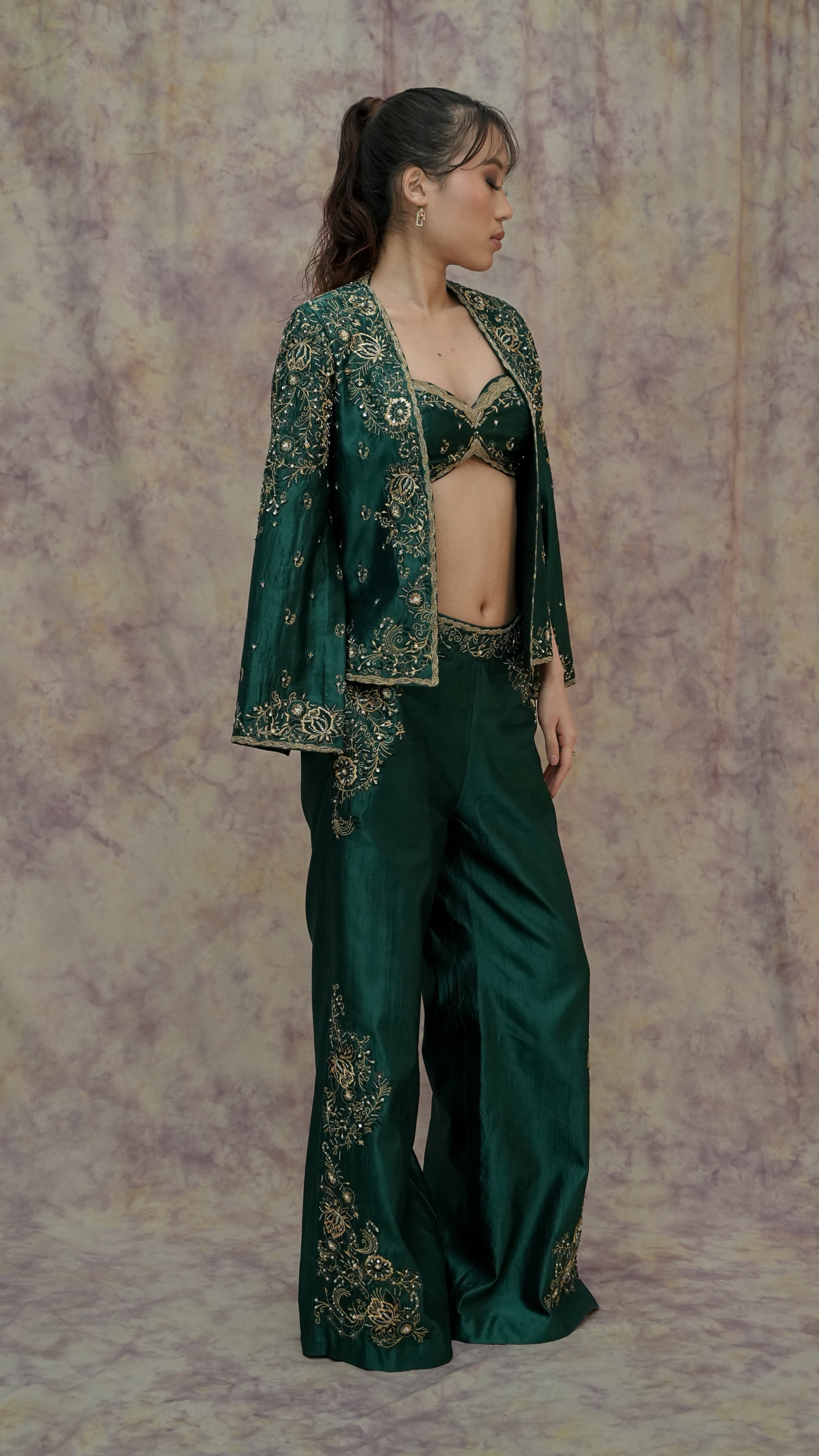 Woman wearing a green embroidered outfit against a patterned background