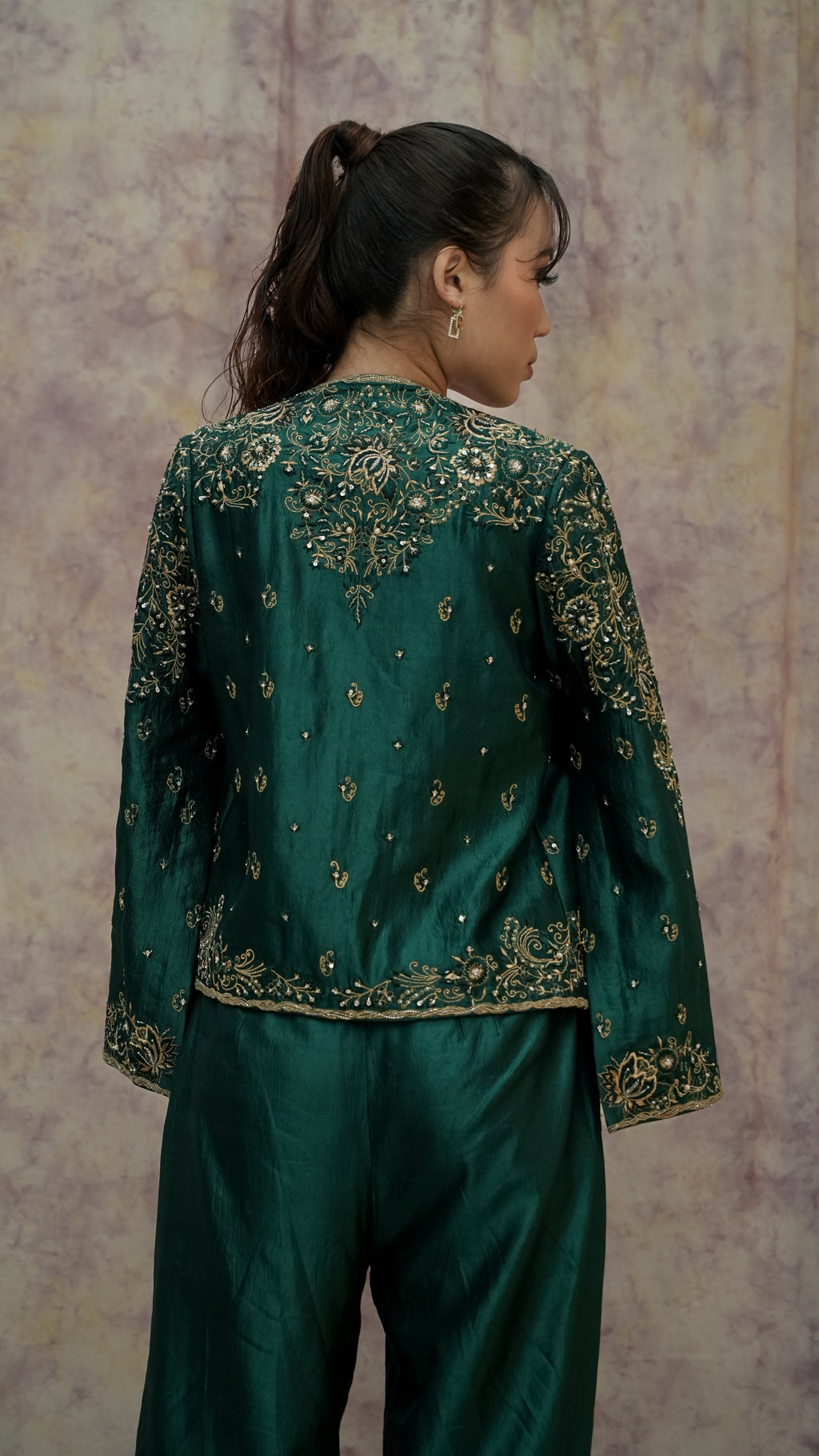Green embroidered traditional outfit with a textured wall background