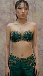 Woman wearing a green embroidered top and skirt against a textured wall.