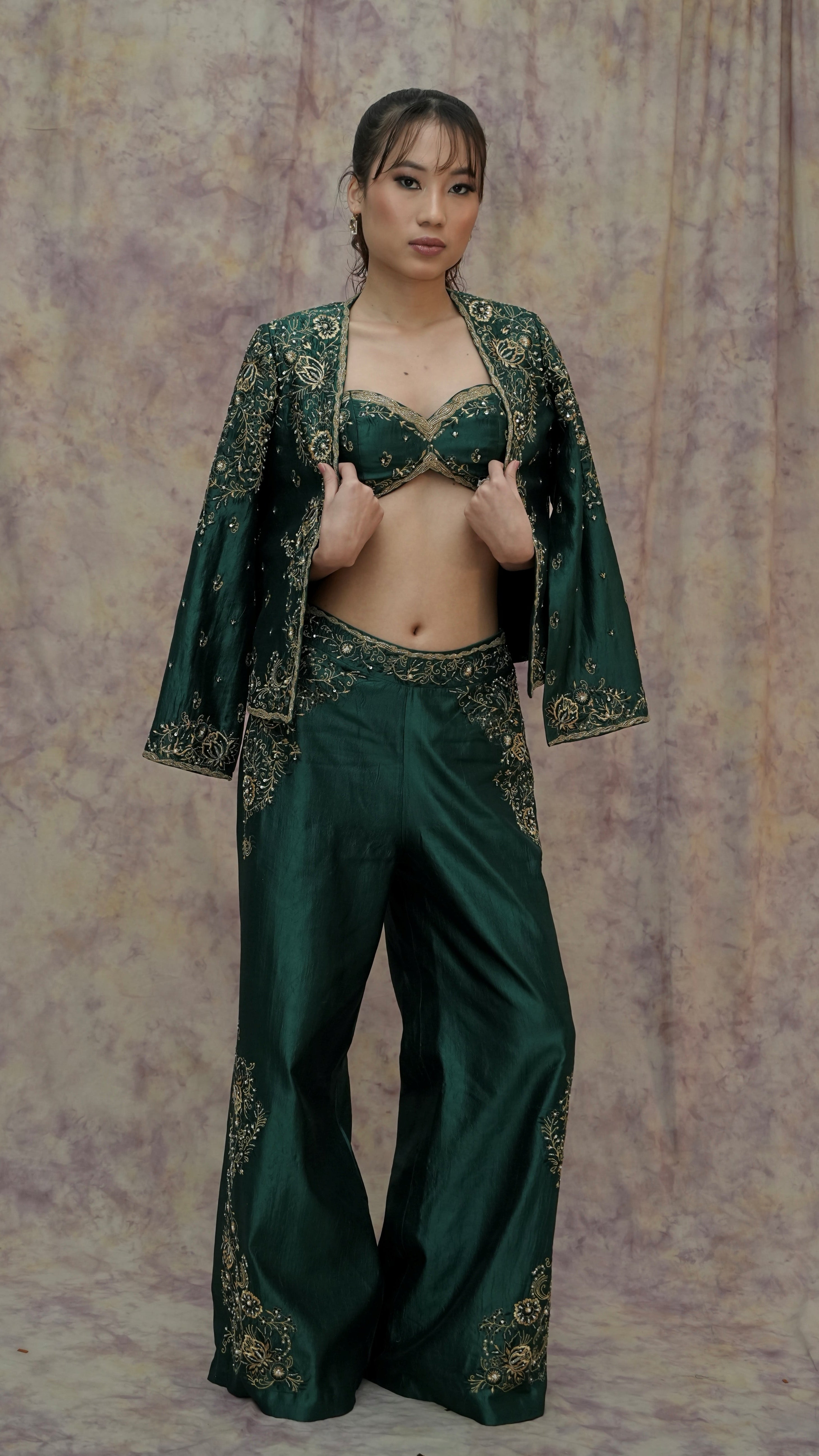 Woman wearing a green embroidered outfit against a textured wall.