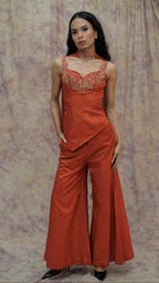 Woman wearing an orange jumpsuit with floral lace details against a patterned backdrop