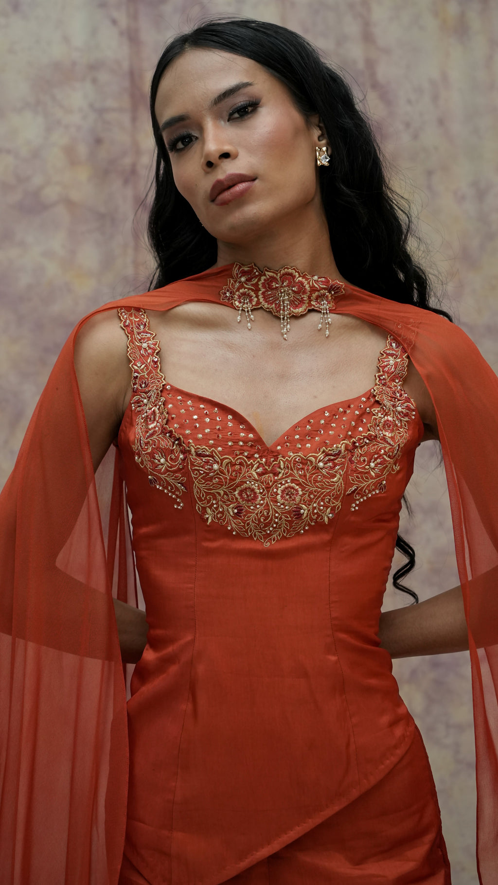 Woman wearing an orange dress with intricate detailing and a matching shawl against a neutral background