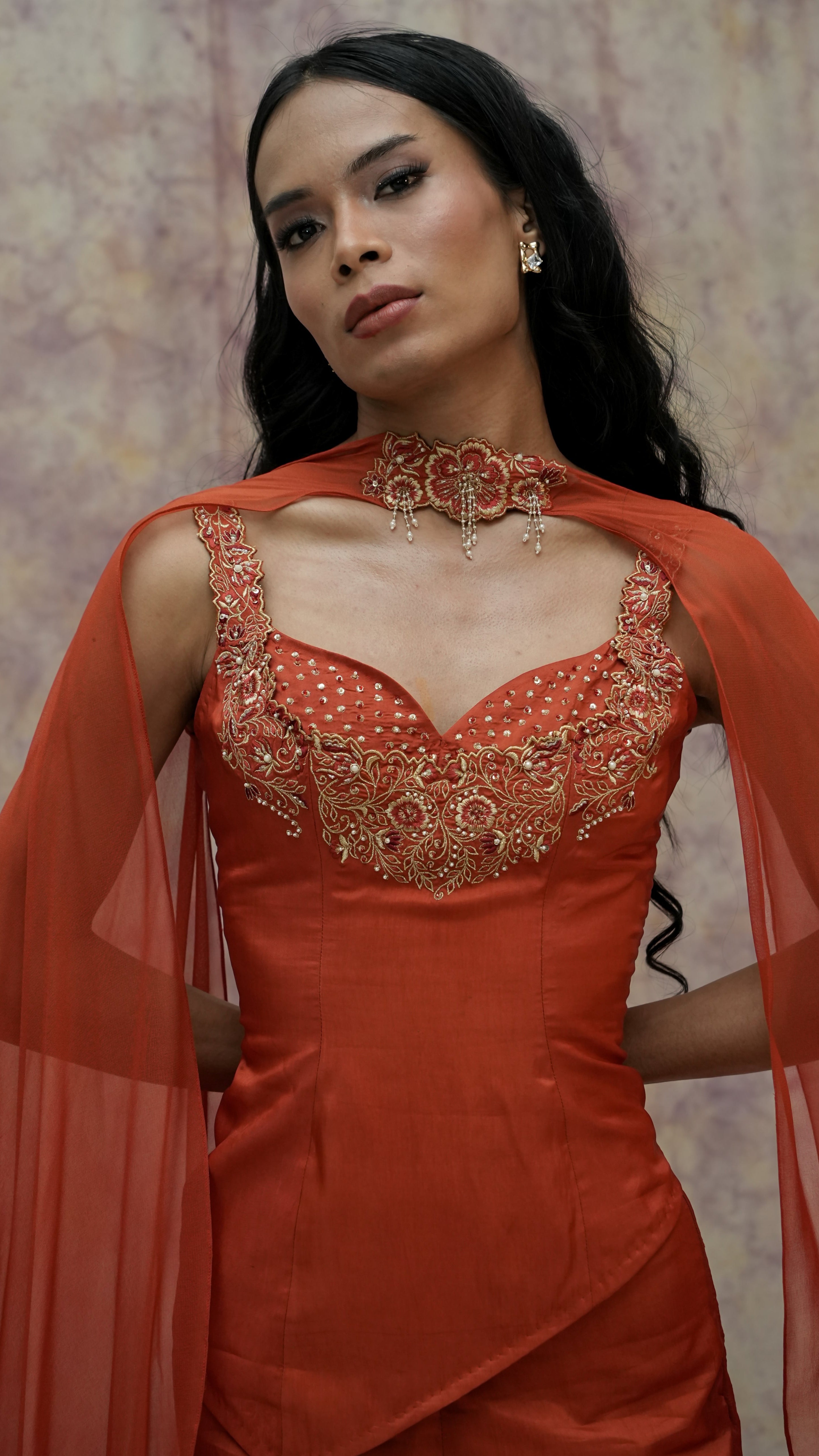 Woman wearing an orange dress with intricate detailing and a matching shawl against a neutral background