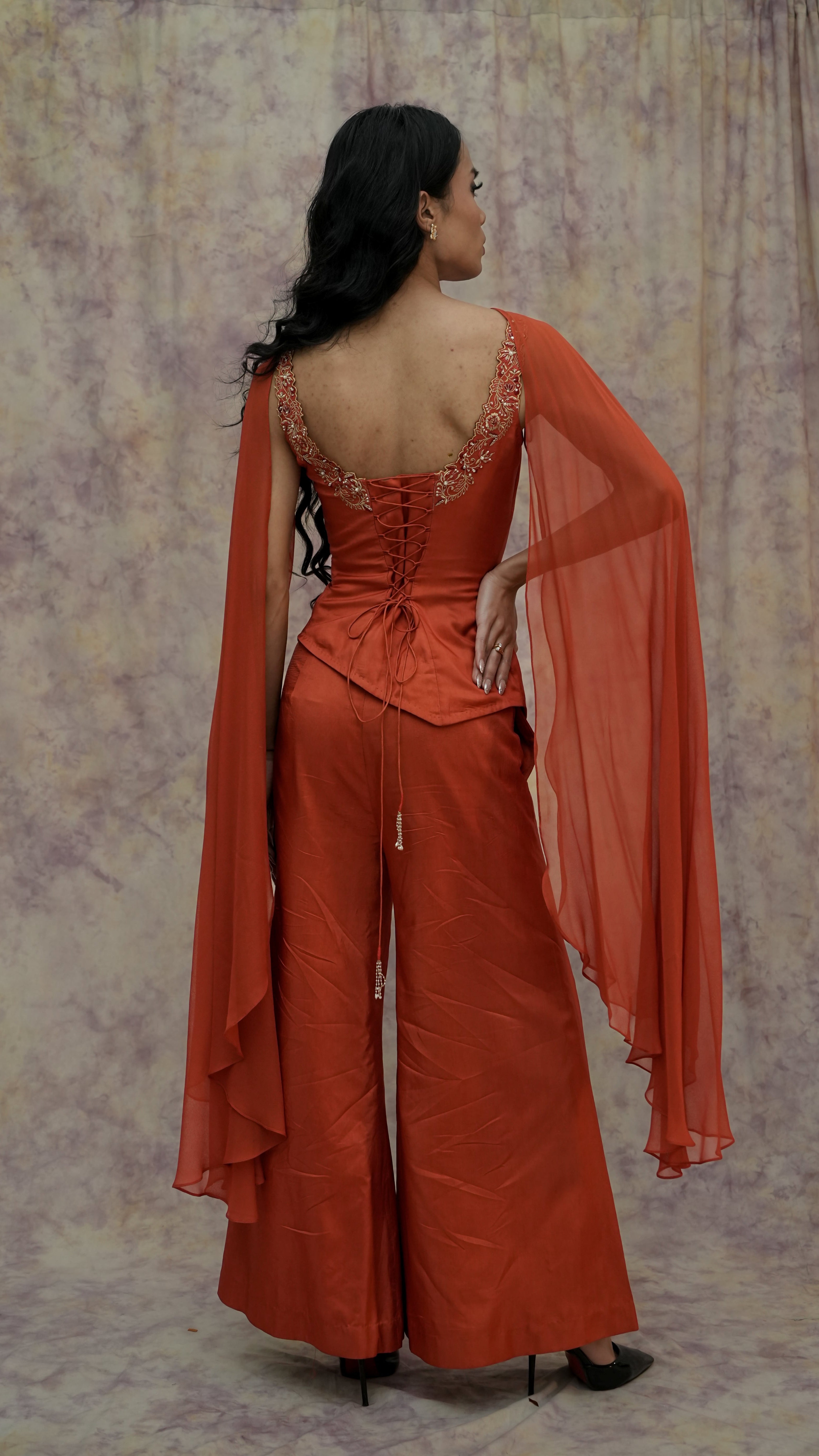 Woman wearing an orange outfit with a sheer dupatta against a patterned backdrop