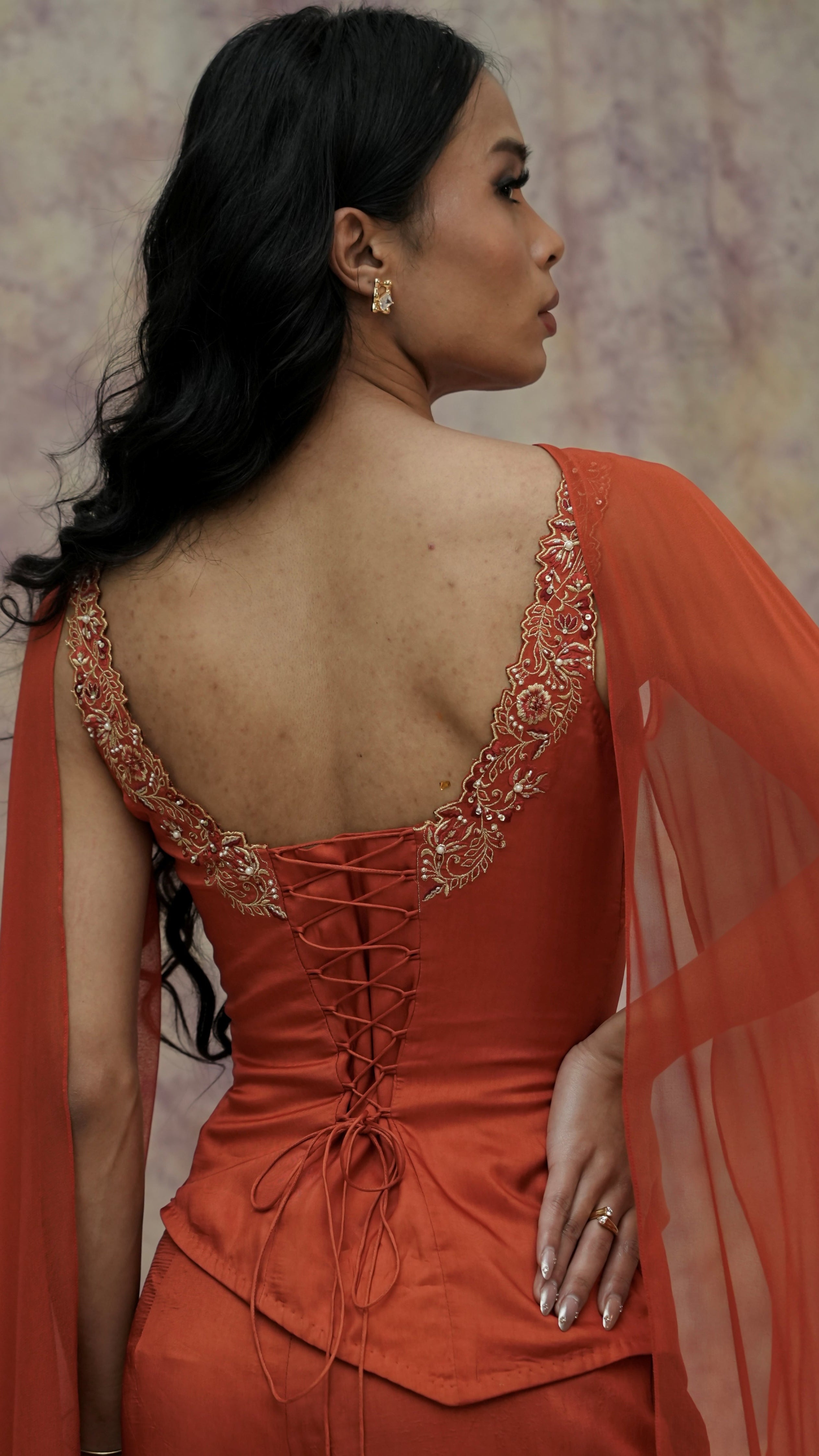 Woman wearing an orange dress with intricate detailing and a sheer overlay against a neutral background
