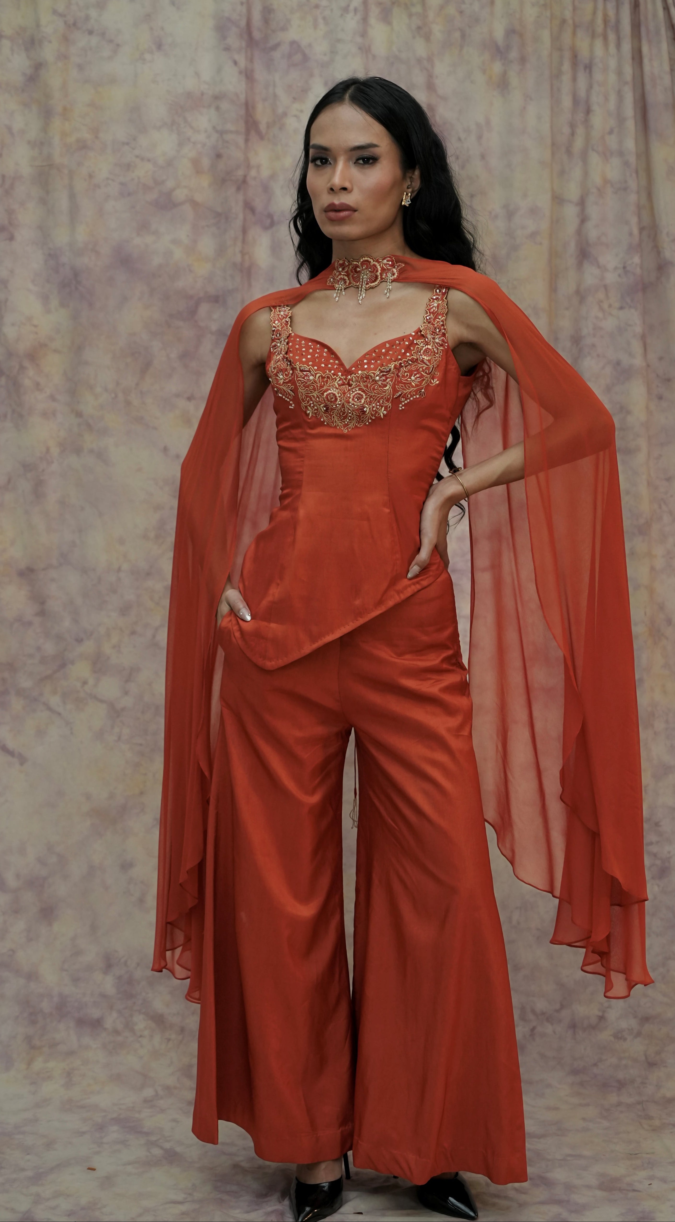 Woman wearing an orange outfit with a sheer overlay against a patterned background