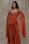 Woman wearing an orange outfit with a cape against a textured wall.