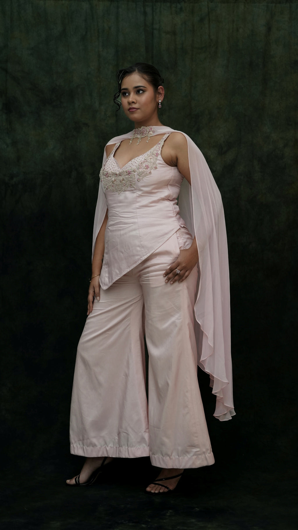 Woman wearing a light pink saree with a dark green background