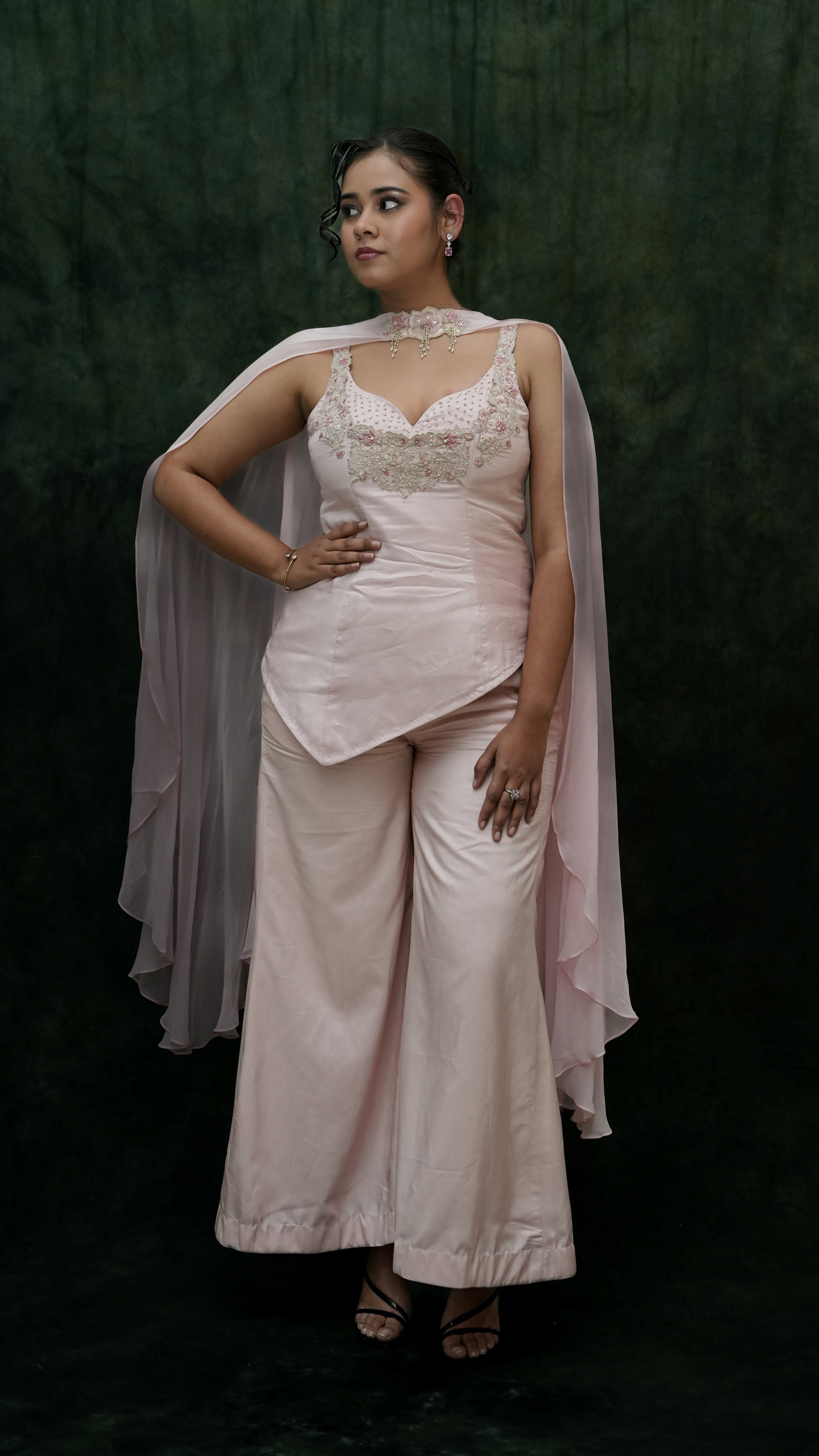 Woman wearing a light pink traditional outfit with a dark green background