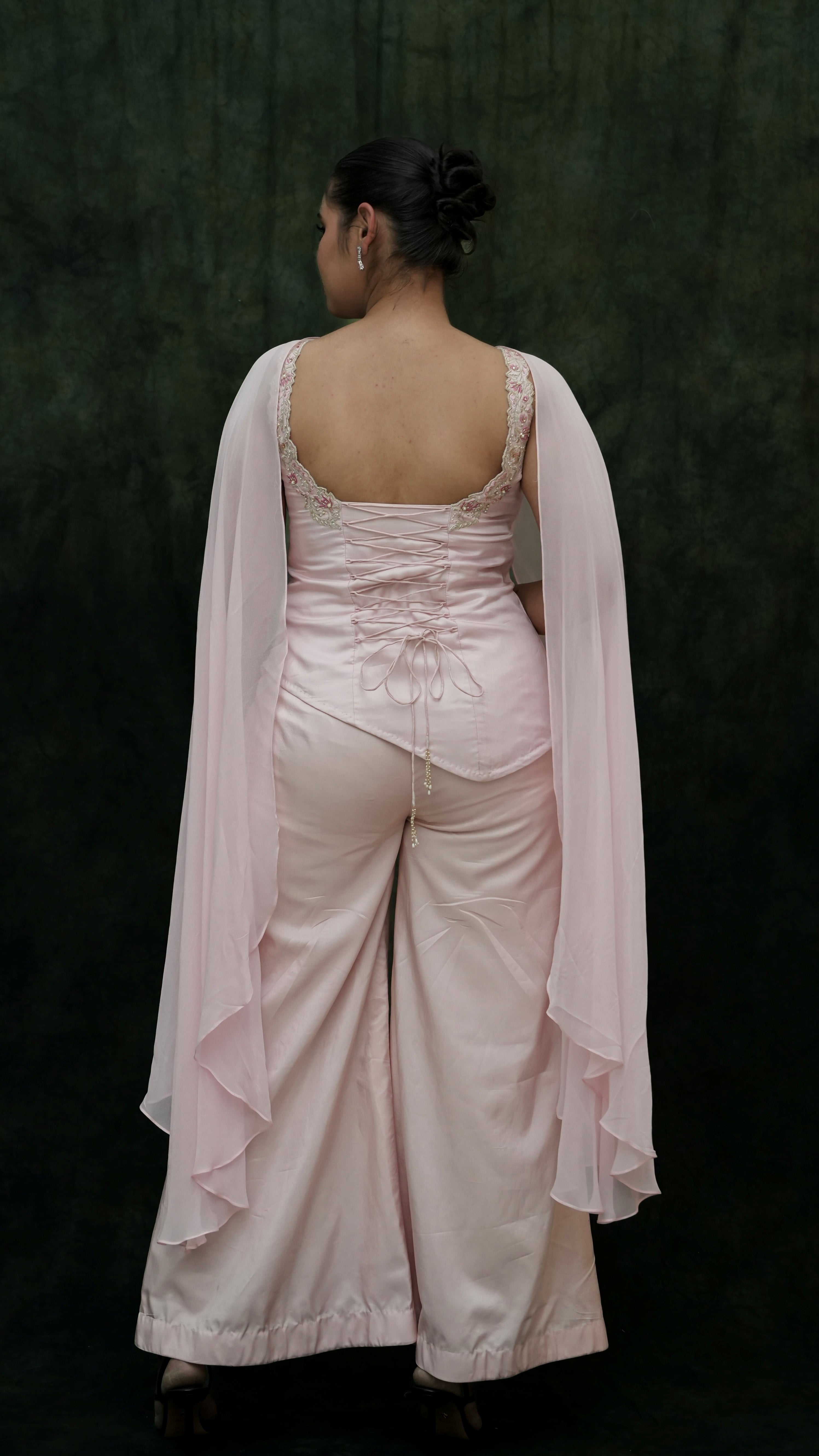 Person wearing a light pink saree with a dark background