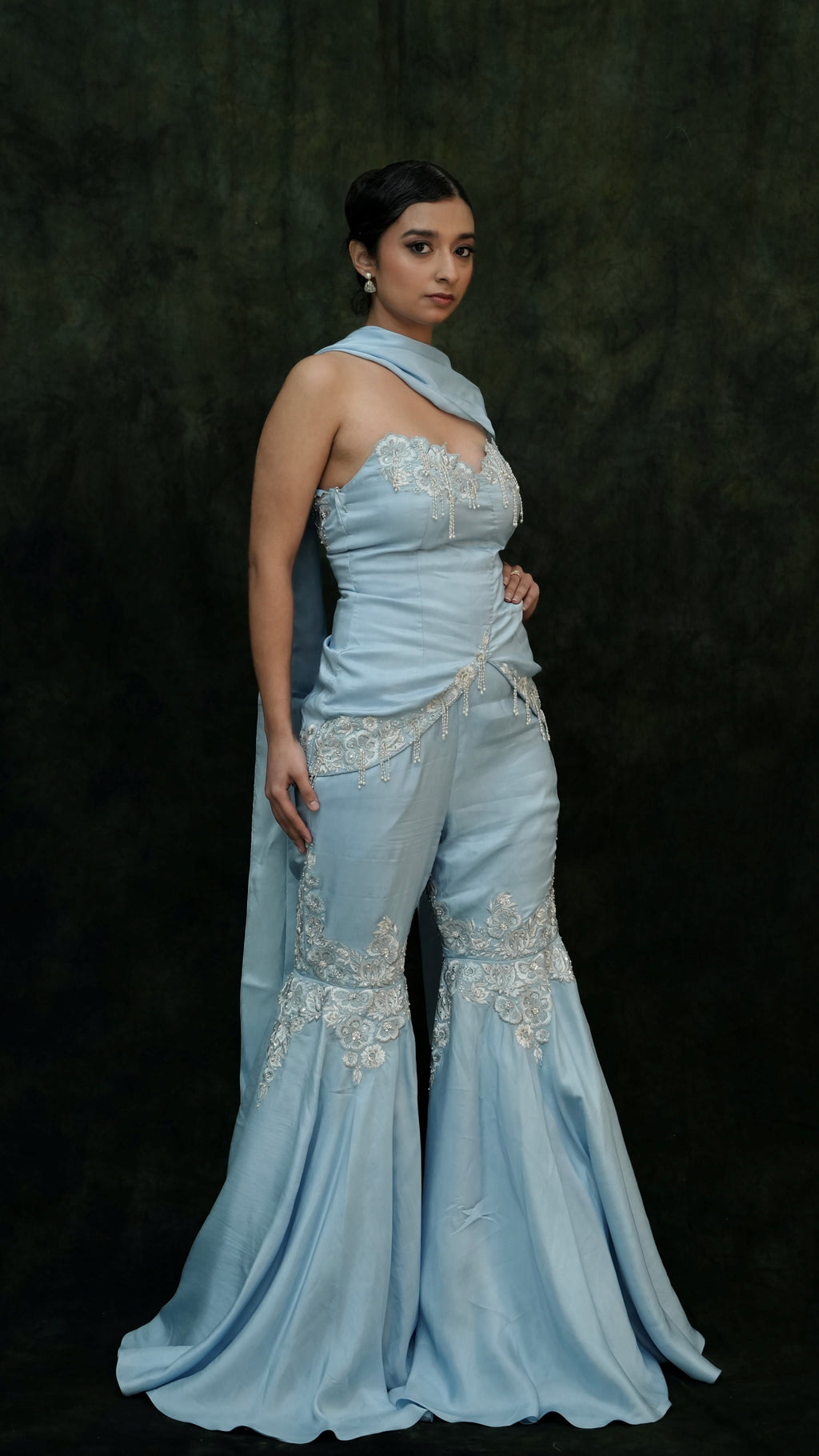 Woman wearing a light blue evening gown with intricate detailing against a dark background