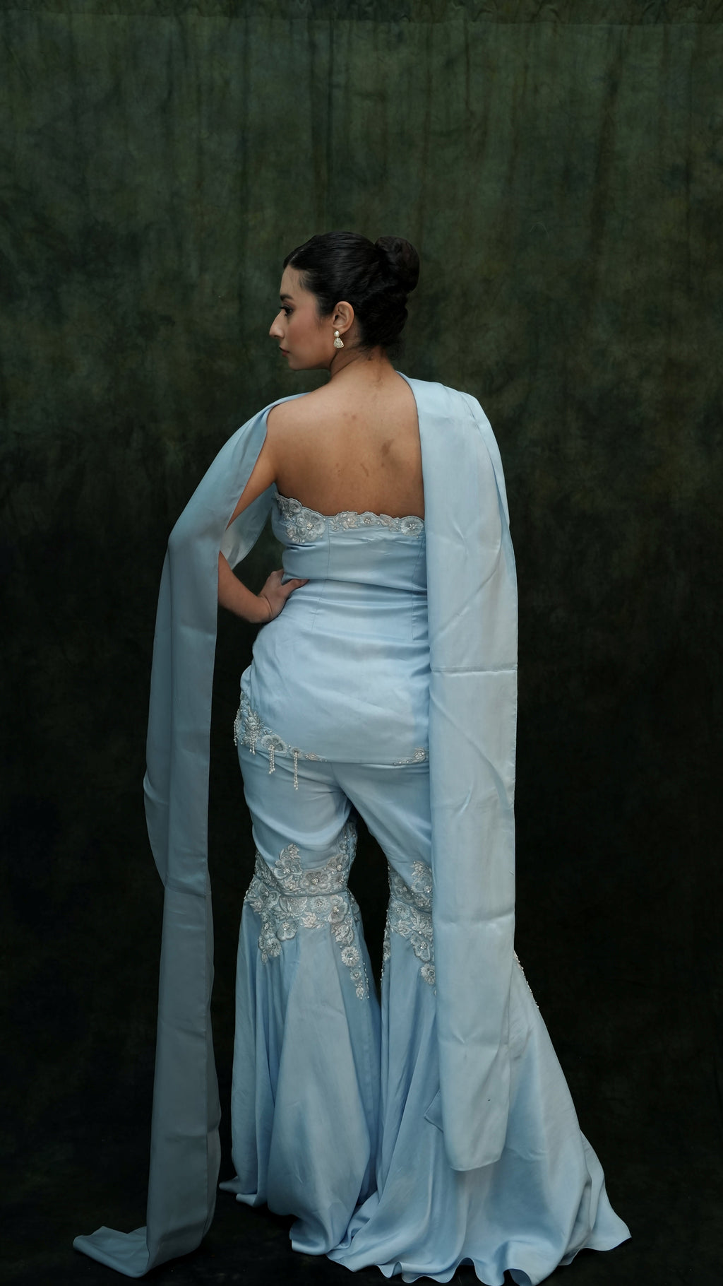 Woman in a light blue evening gown with a long train against a dark background