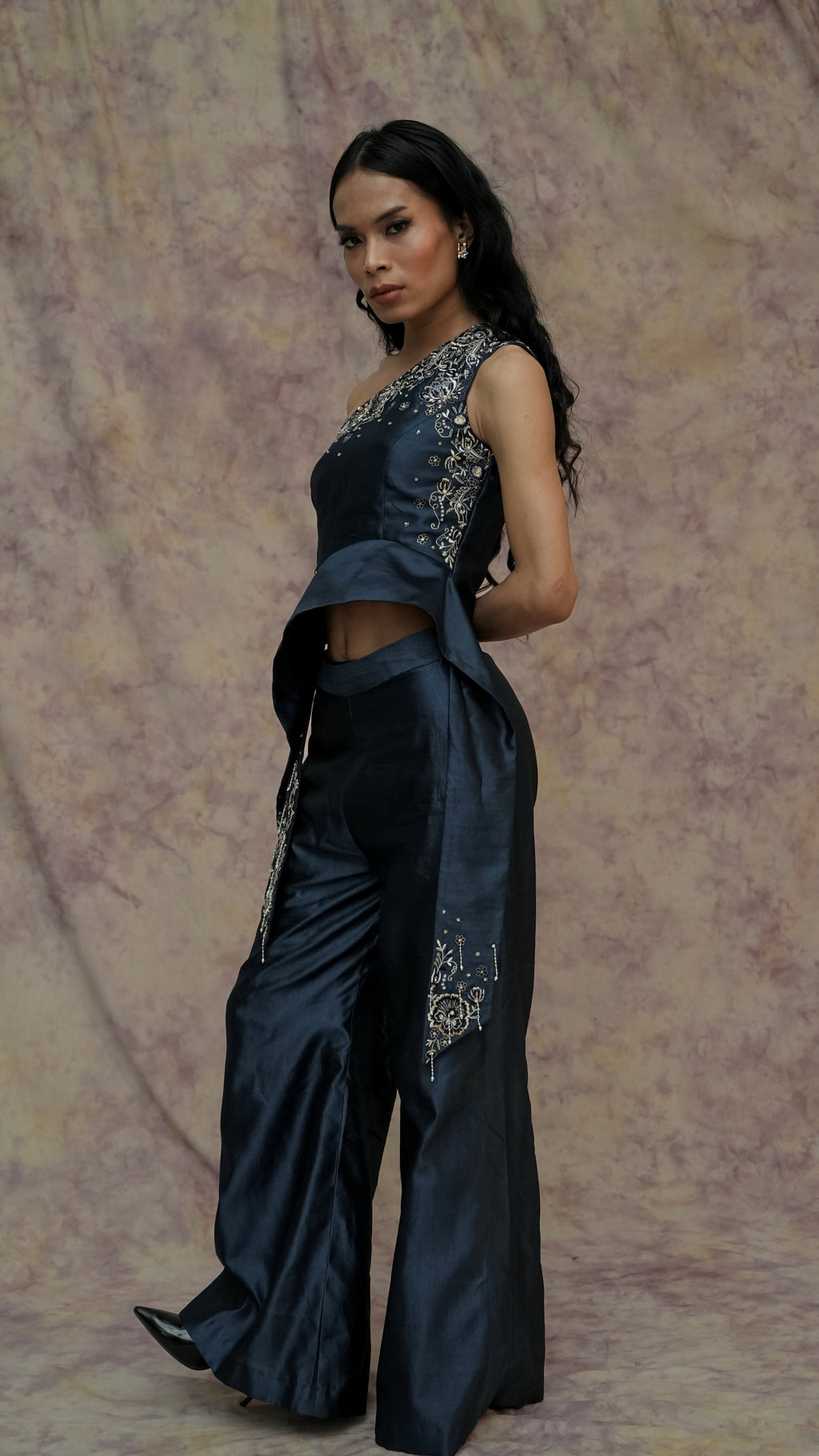 Woman wearing a dark blue saree with silver embroidery against a textured beige background