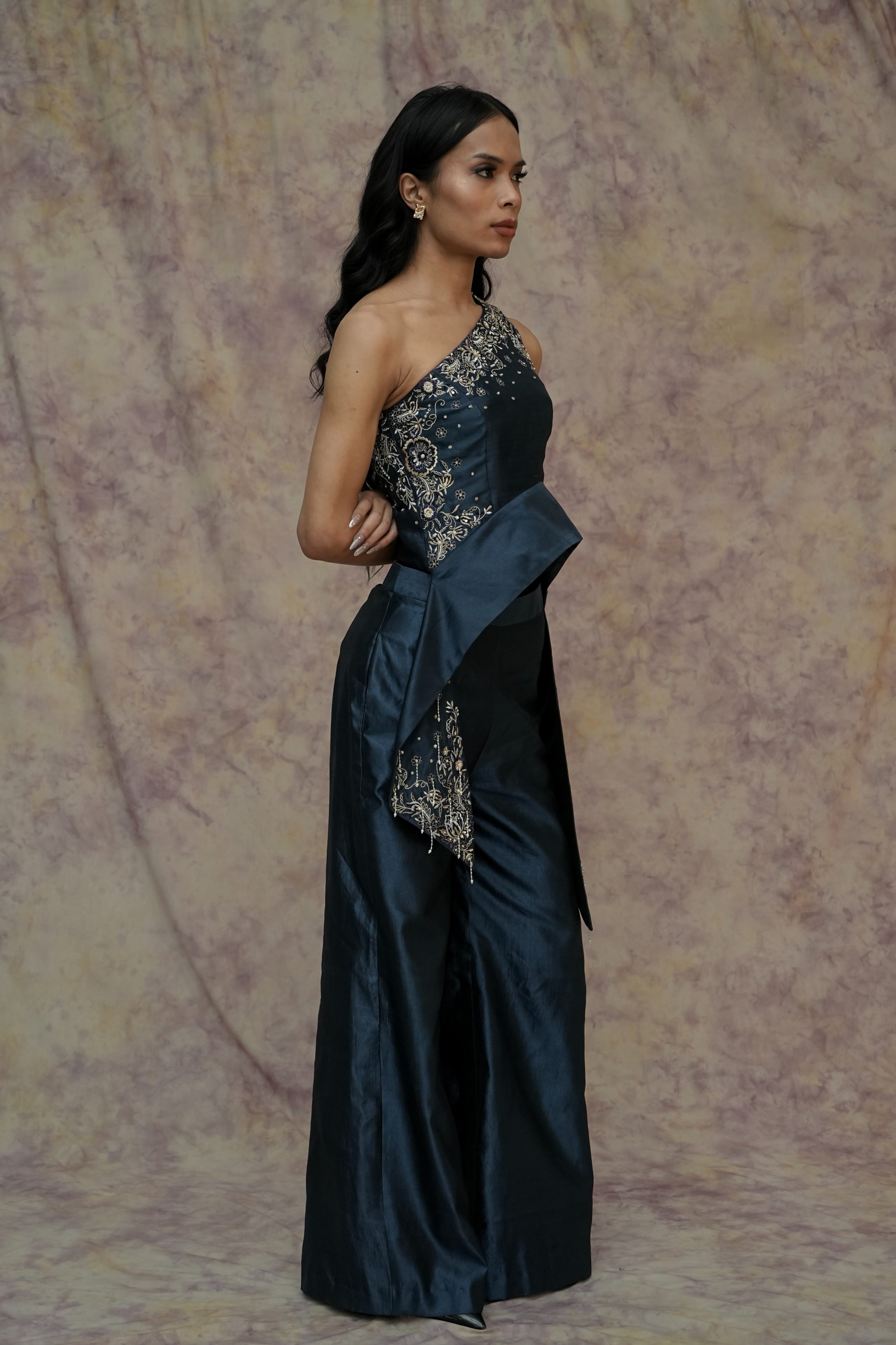 Woman wearing a dark blue evening gown with intricate detailing against a textured beige background