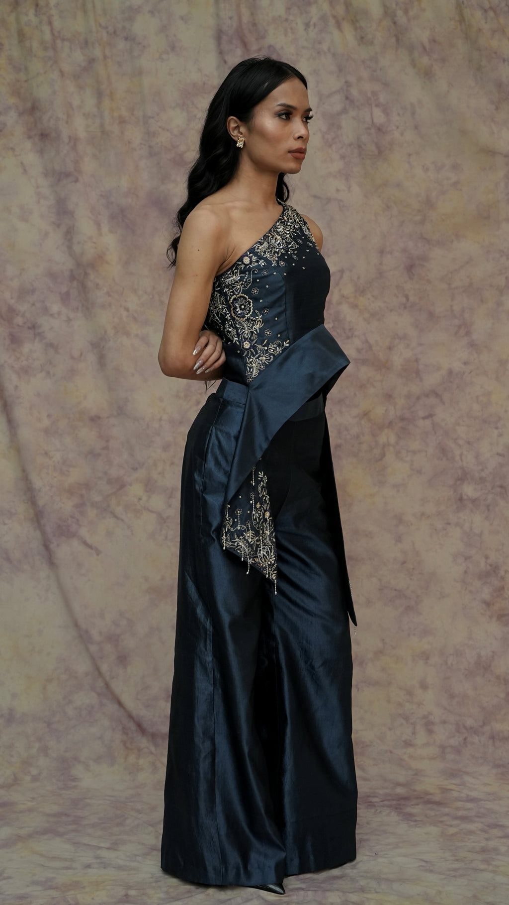Woman wearing a dark blue evening gown with floral embroidery against a textured purple background