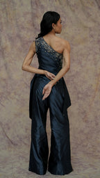 Woman wearing a black one-shoulder jumpsuit with intricate detailing on a textured beige background