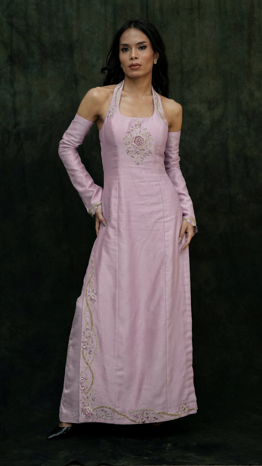 Woman wearing a pink evening gown with intricate detailing on a dark background