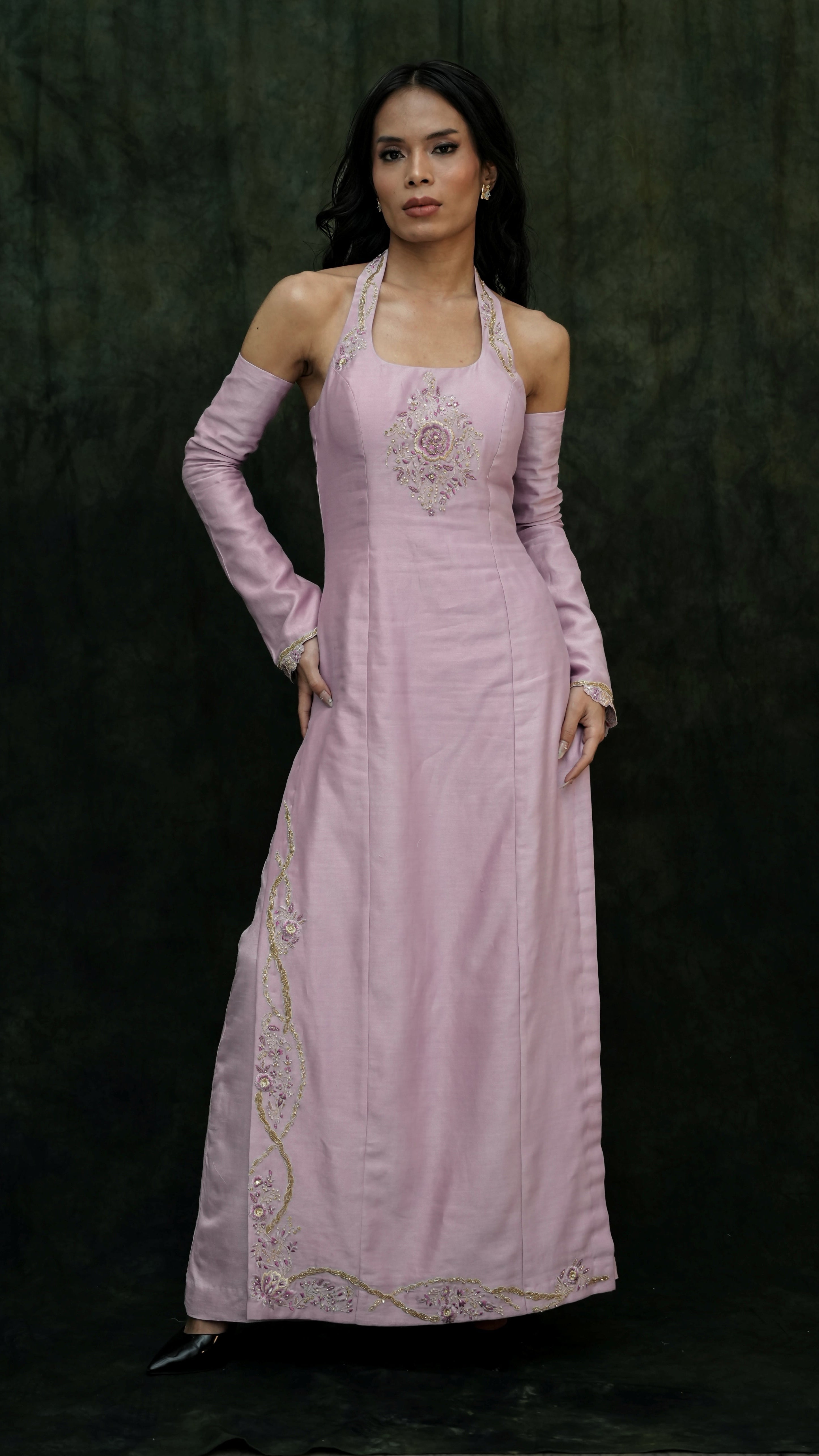 Woman wearing a pink evening gown with intricate detailing on a dark background