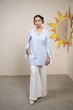 Woman in a light blue shirt and white pants standing in front of a sun art piece.