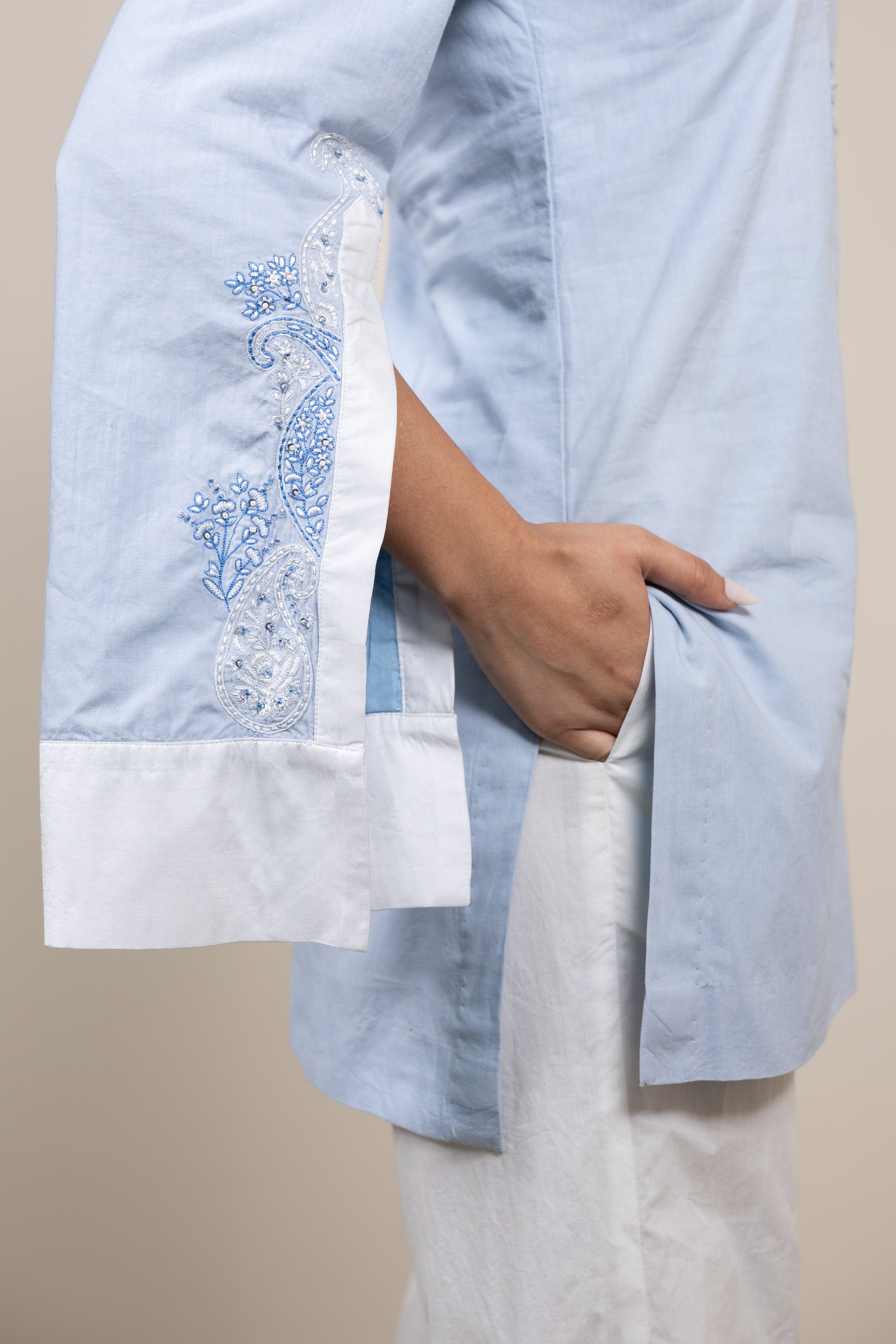 Light blue embroidered top with white pants on a beige background
