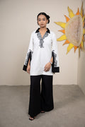 Woman wearing a white and black outfit with decorative elements, standing in front of a sunflower painting.